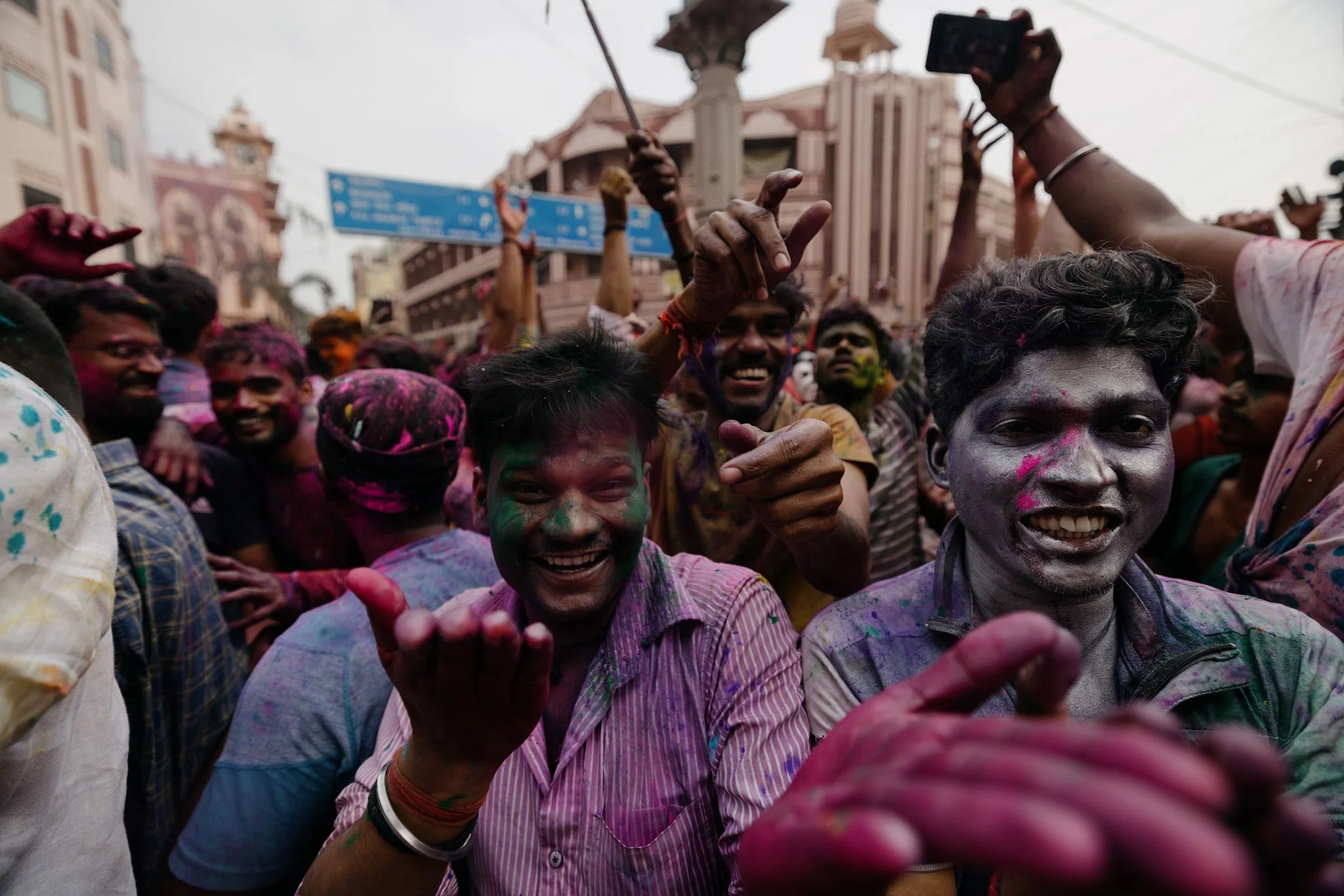 People celebrating Holi festival on the street, covered in colorful powder, smiling and throwing powder at each other.