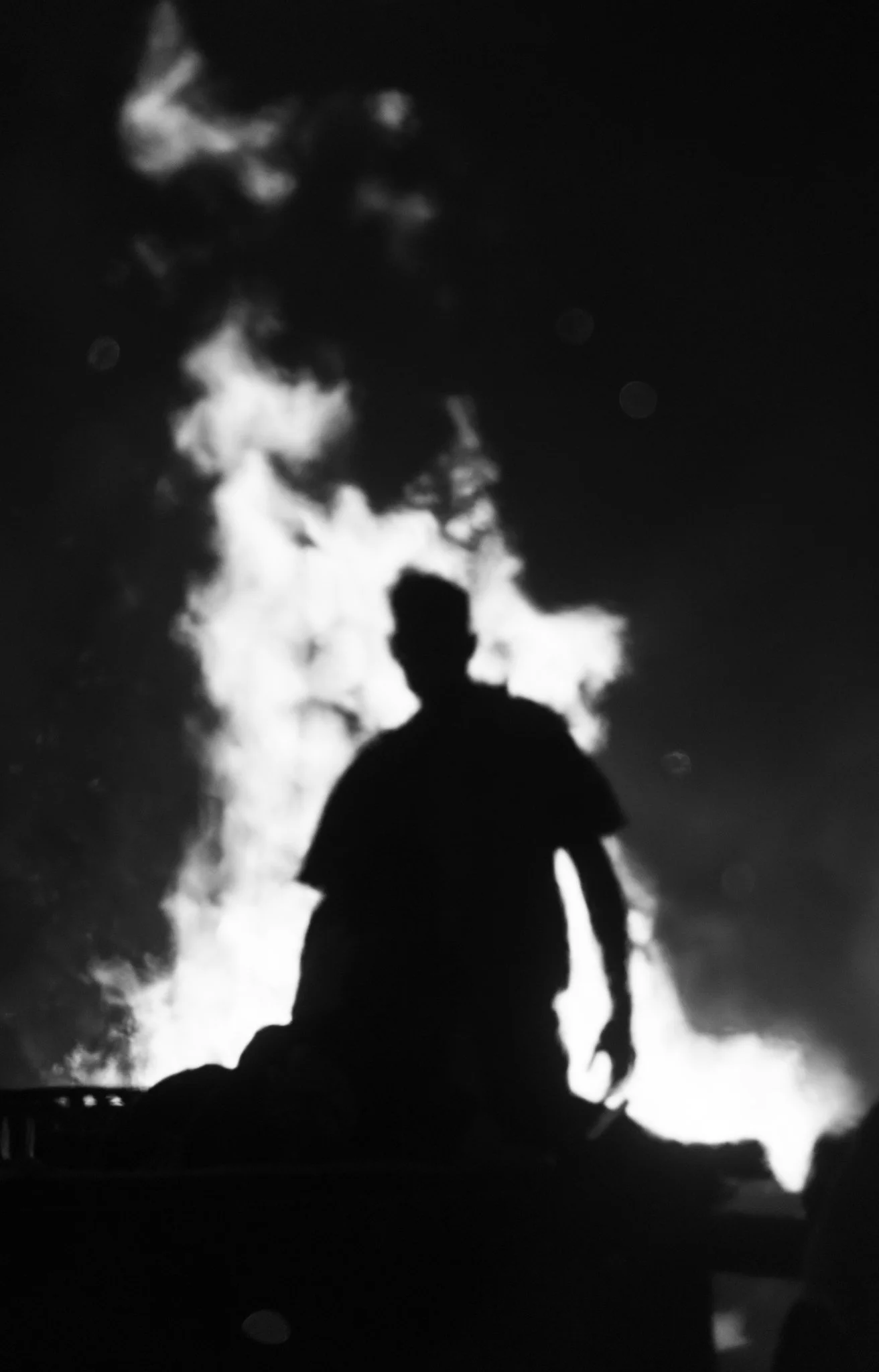 Silhouette of a person standing at night with a cloudy sky illuminated behind them.