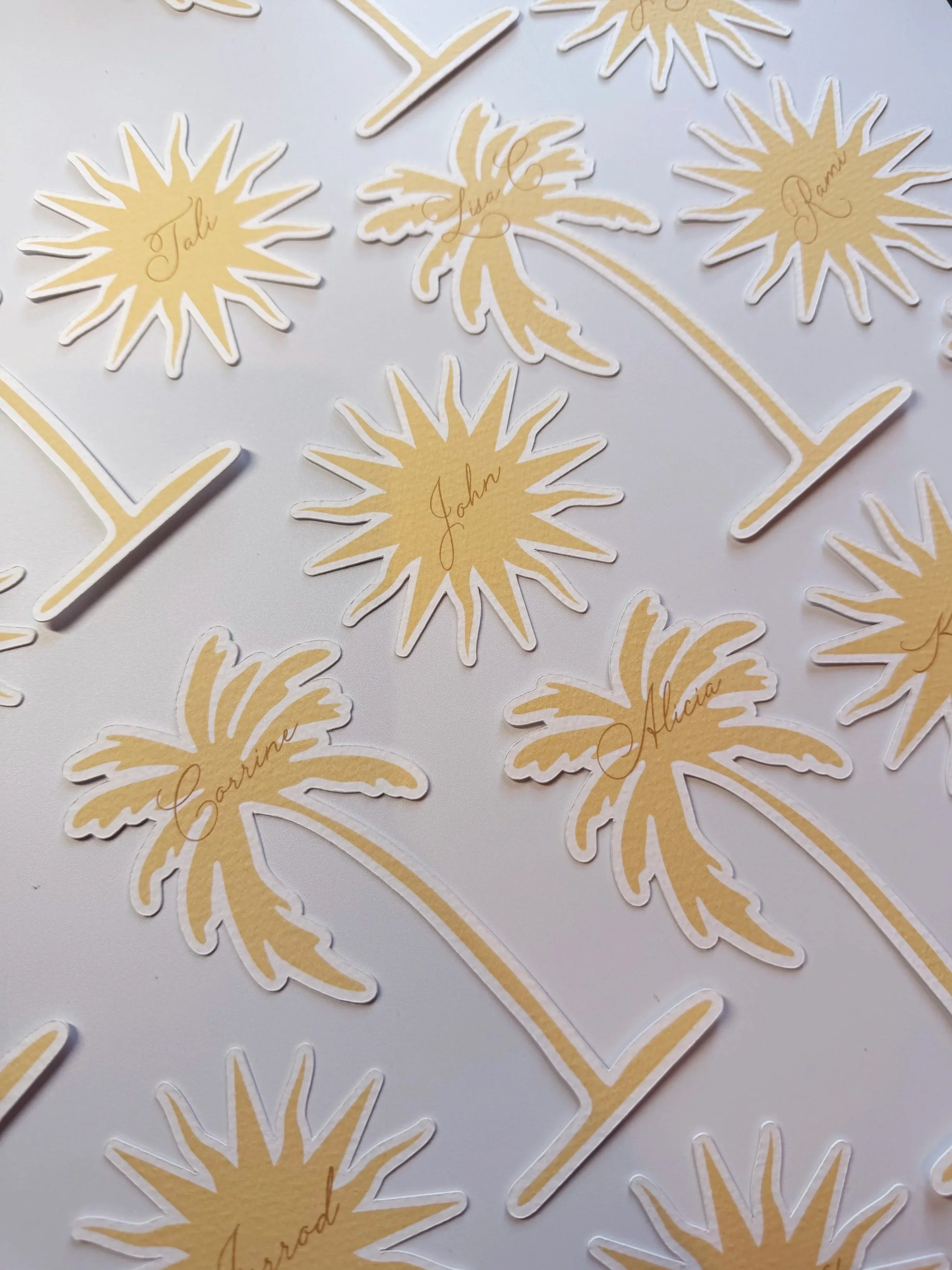 Decorative stickers of yellow and white palm trees and sunburst shapes with names written in cursive, scattered on a white background.