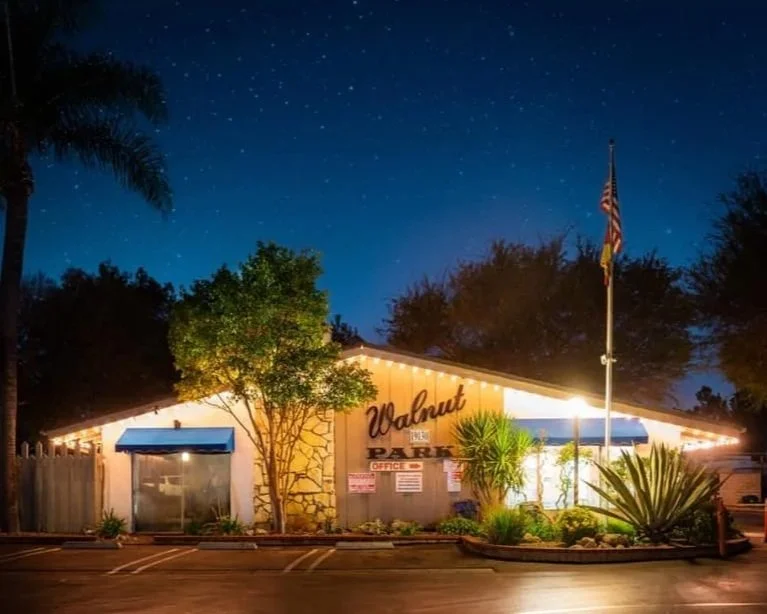 Night view of Walnut RV Park with an illuminated building, trees, a flagpole, and stars in the sky.