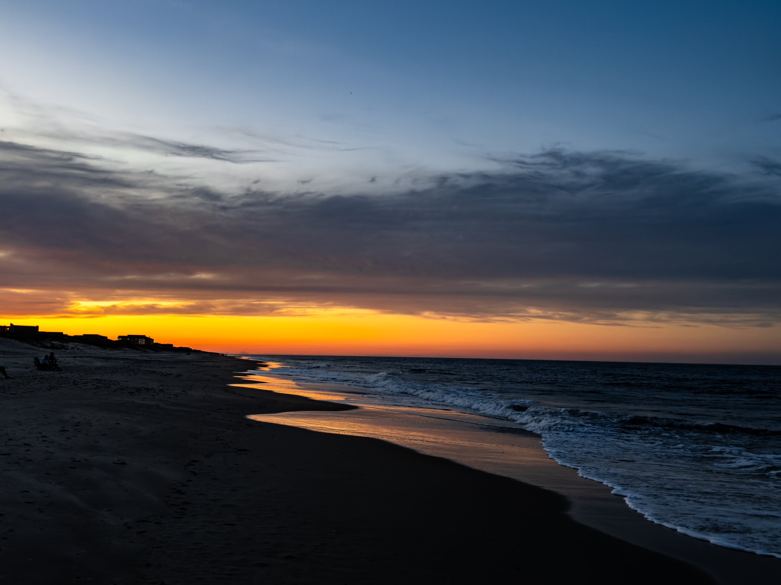 Sunset over the ocean with dark clouds and a sandy beach in the foreground.