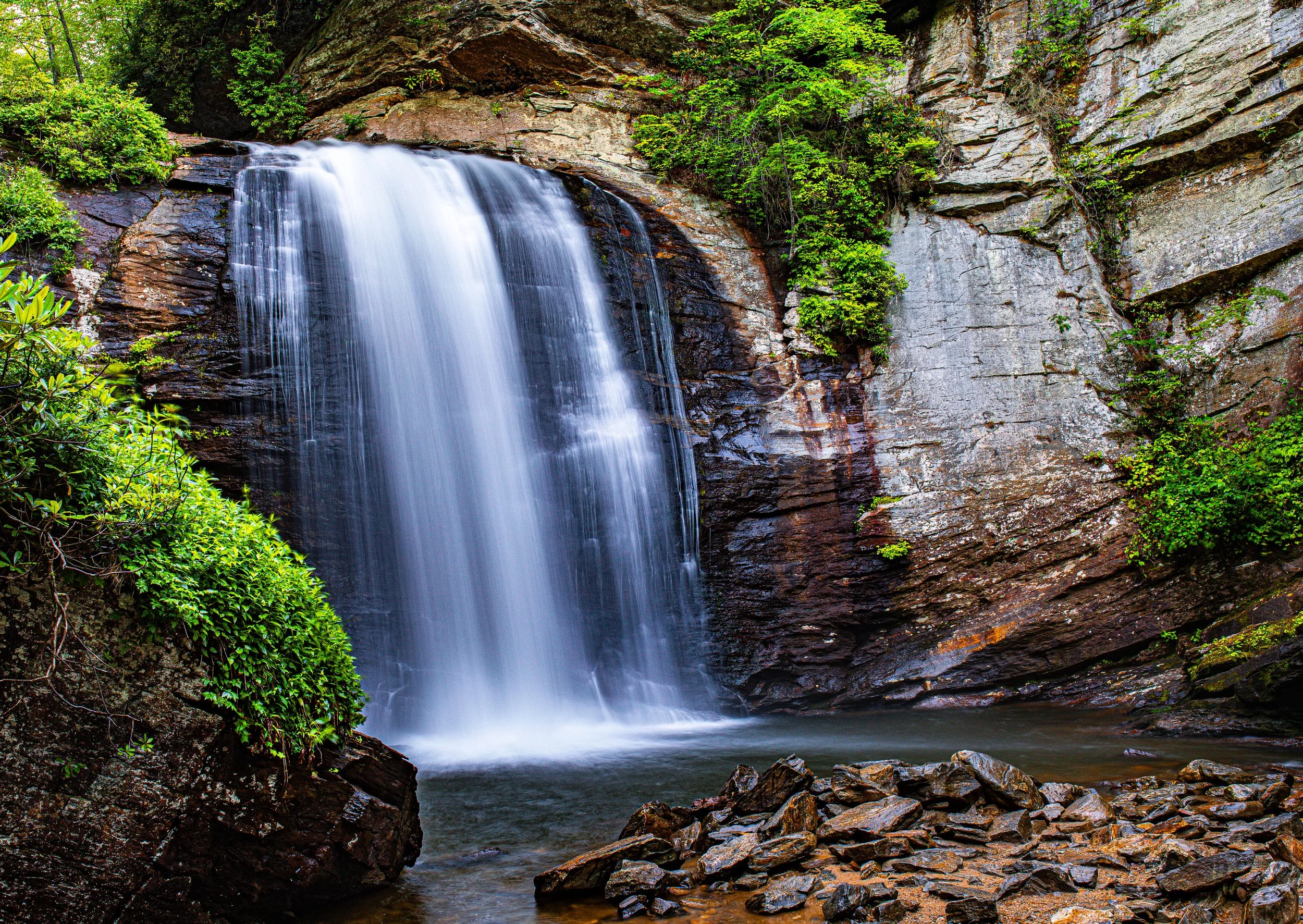 Waterfall flowing over rocky cliffs surrounded by green trees and bushes in a forest setting.