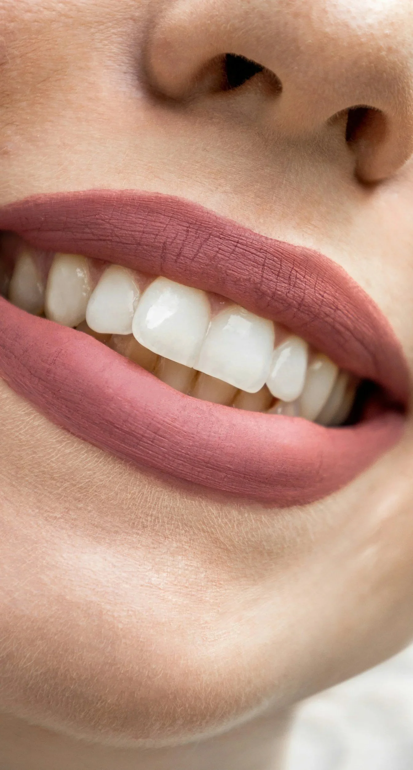 Nahaufnahme eines lächelnden Gesichts mit roten Lippen, weißen Zähnen und einer Nasenöffnung.