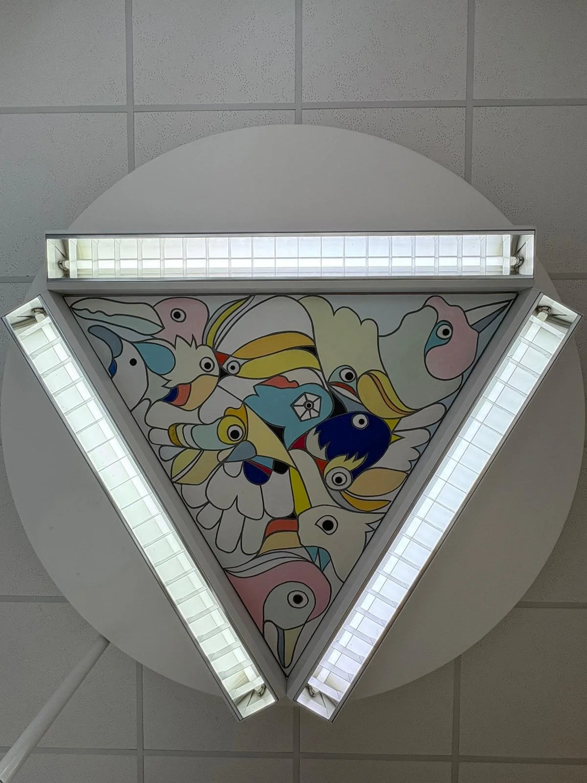 Bunte Wandmalerei mit Vögeln auf der Decke eines Raums, umrahmt von vier Helligkeitsleuchten, gesehen von unten.