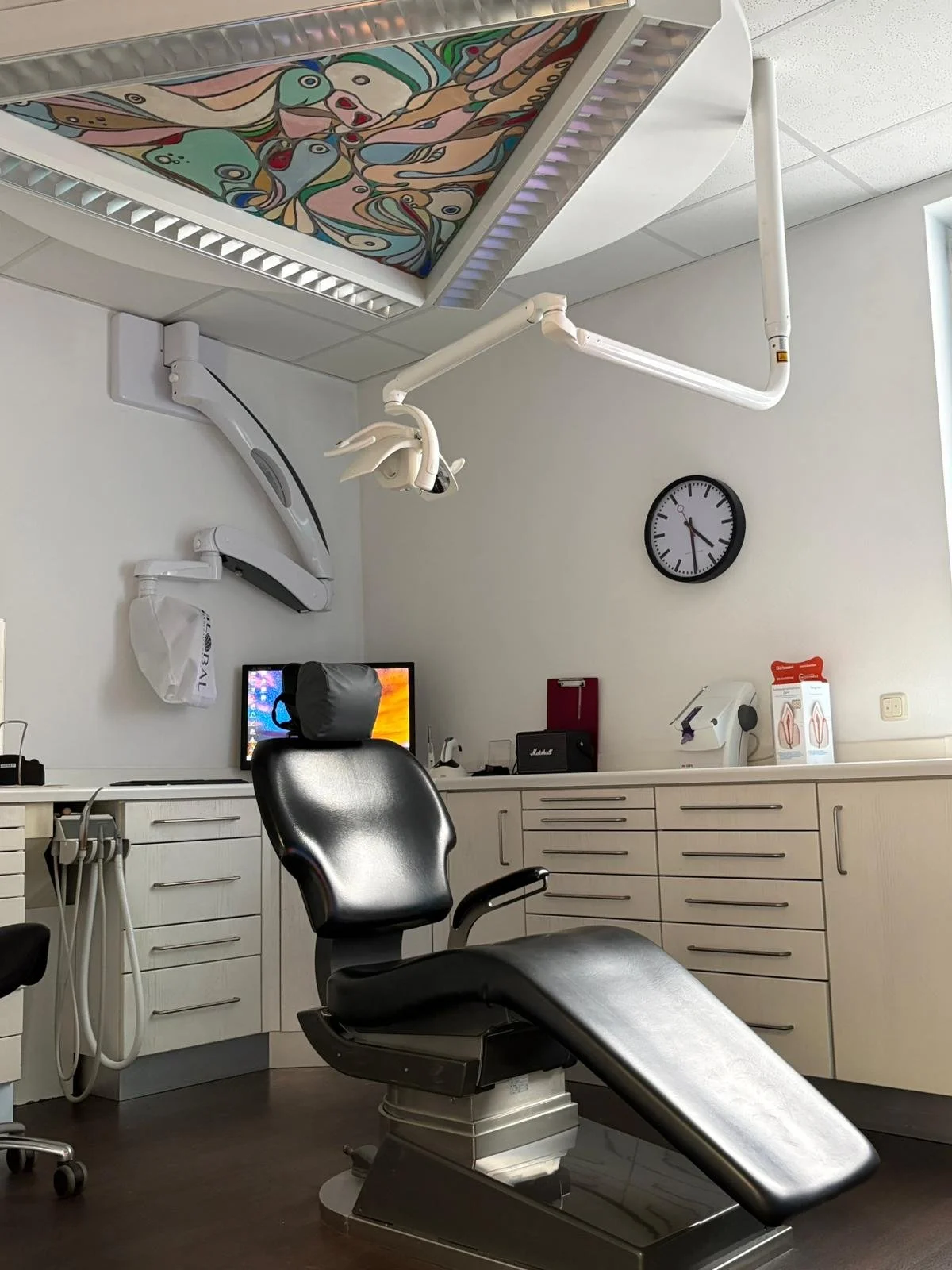 Ein modernes Zahnarztzimmer mit einem Behandlungsstuhl, medizinischen Geräten, einem Computer und einem Wand-Uhr.