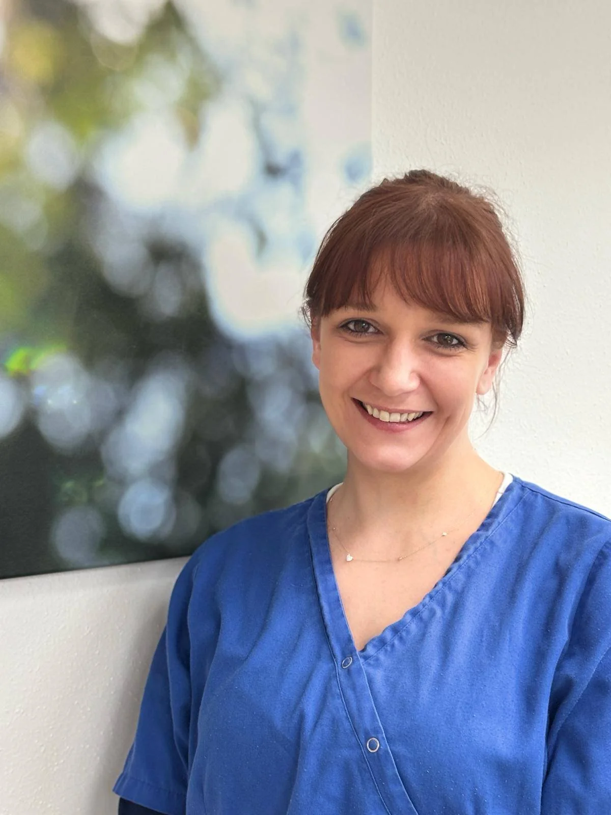 Eine Frau in blauer medizinischer Kitt getanzt vor einer Wand mit einem Kunstwerk, das blauer Himmel und grüne Blätter zeigt.