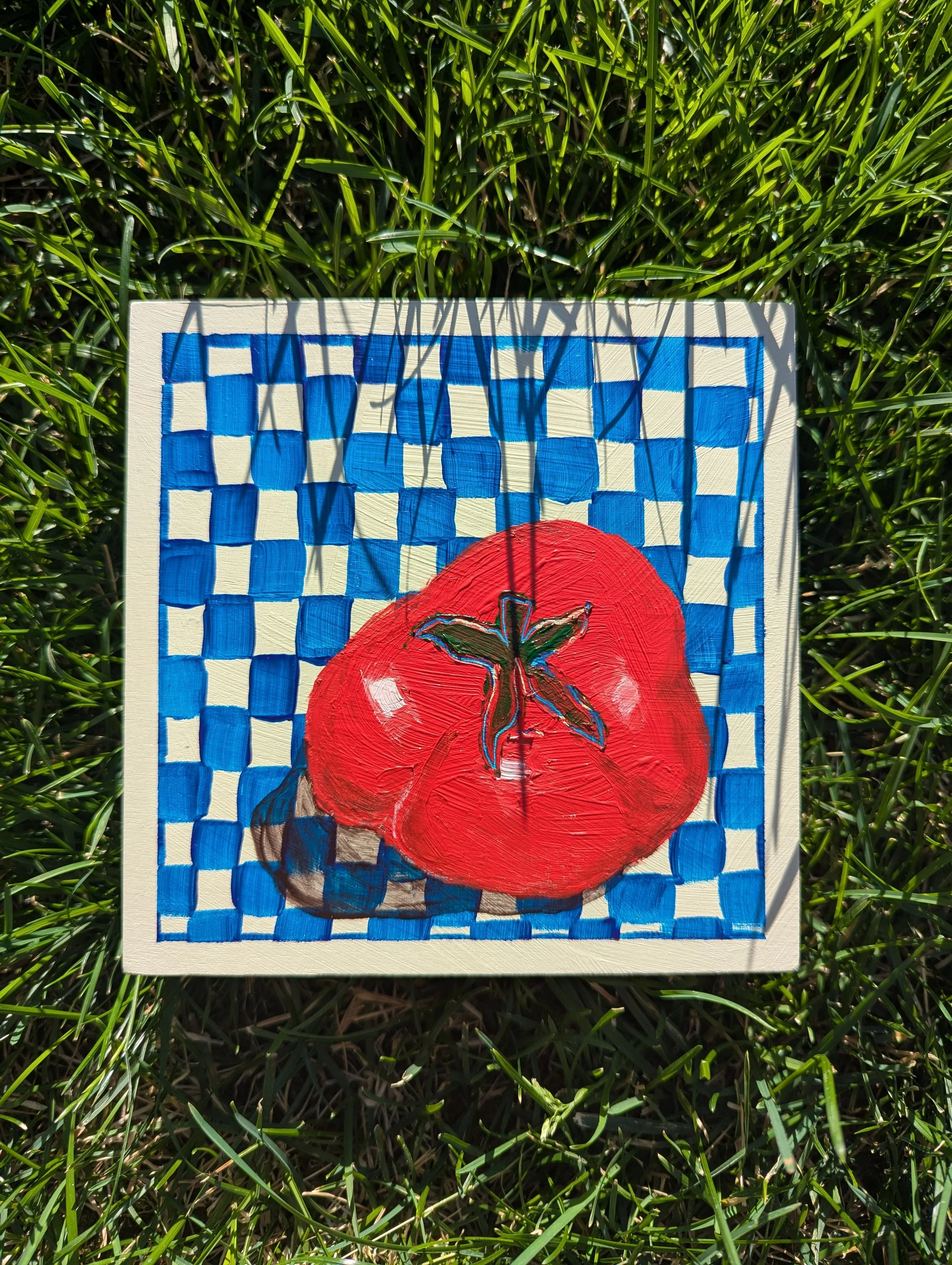 Painting of a large red tomato with a green stem on a checkered blue and white background, placed on green grass.