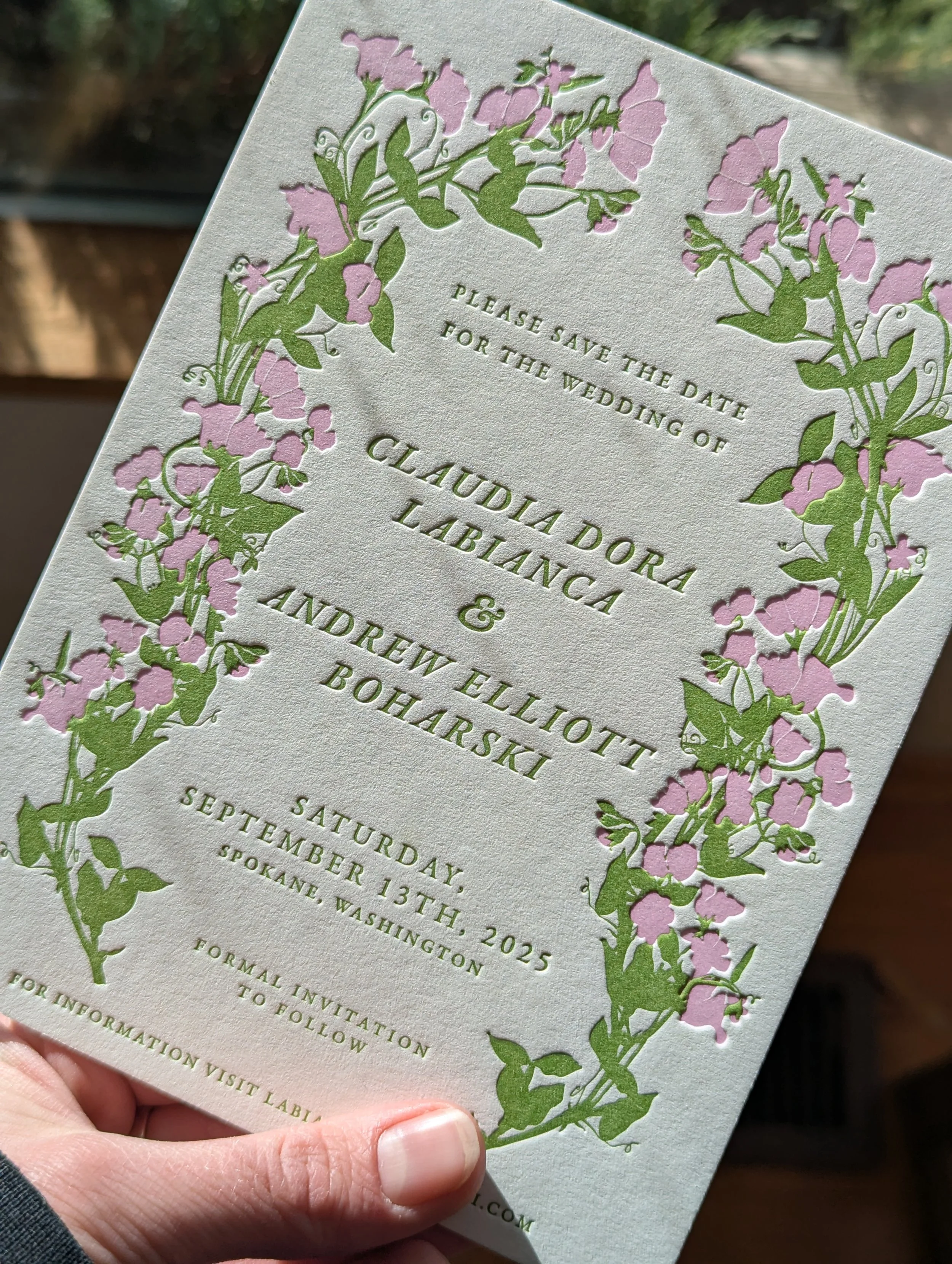 Wedding save-the-date card with floral border of pink flowers and green leaves, text includes vows, names of the couple, and wedding date in Spokane, Washington.