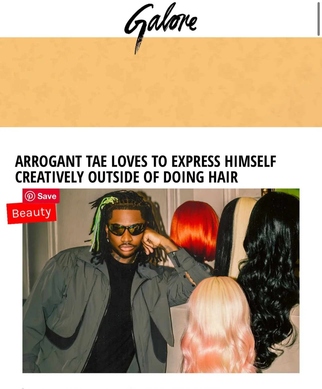 A man with dreadlocks wearing sunglasses and a jacket, standing in front of colorful wigs.