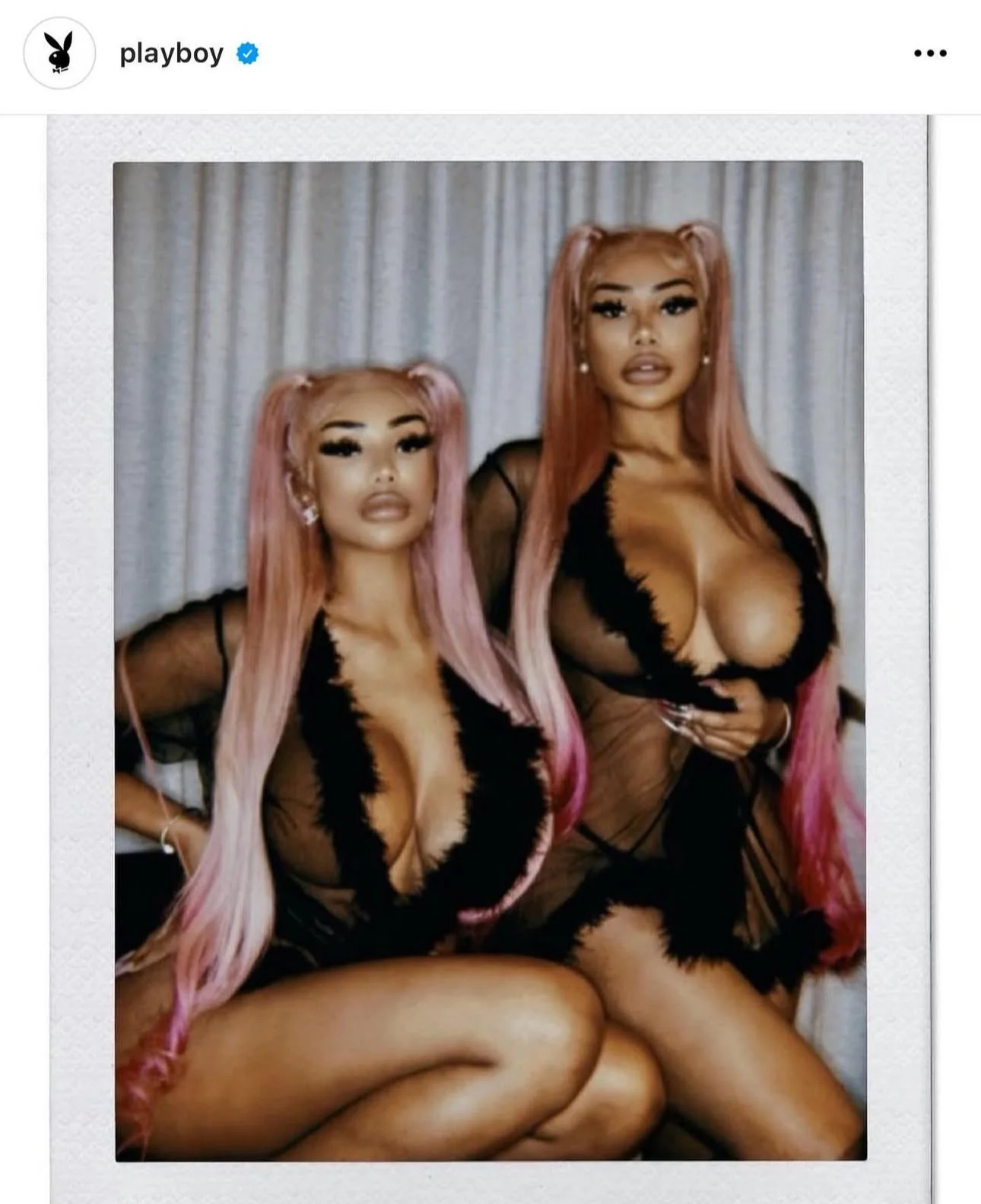Two women with pink hair in black lace lingerie posing in front of a curtain.