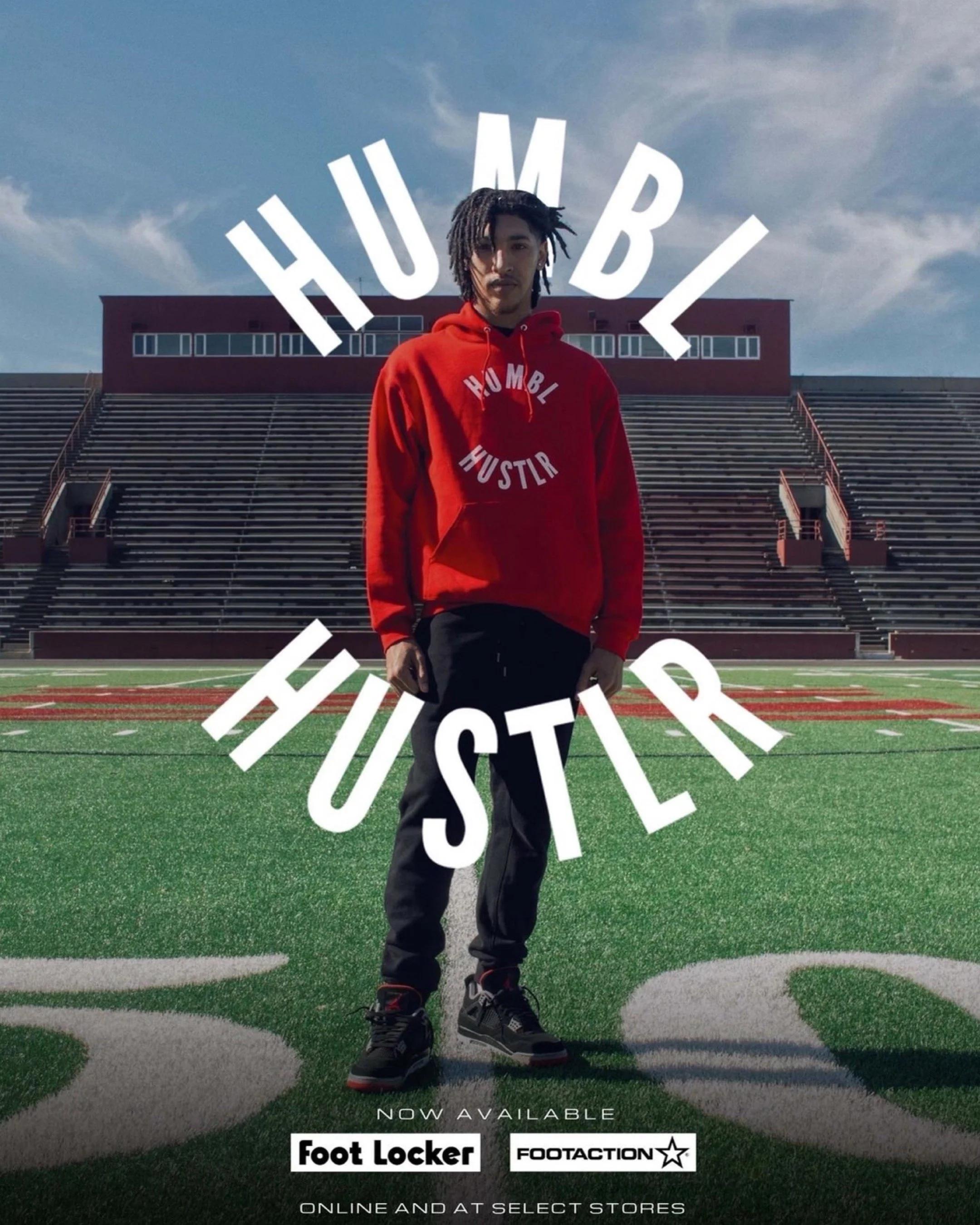 A young man standing on a football field in front of stadium seats, wearing a red hoodie with white text, and promotional text overlays for Foot Locker and Footaction.