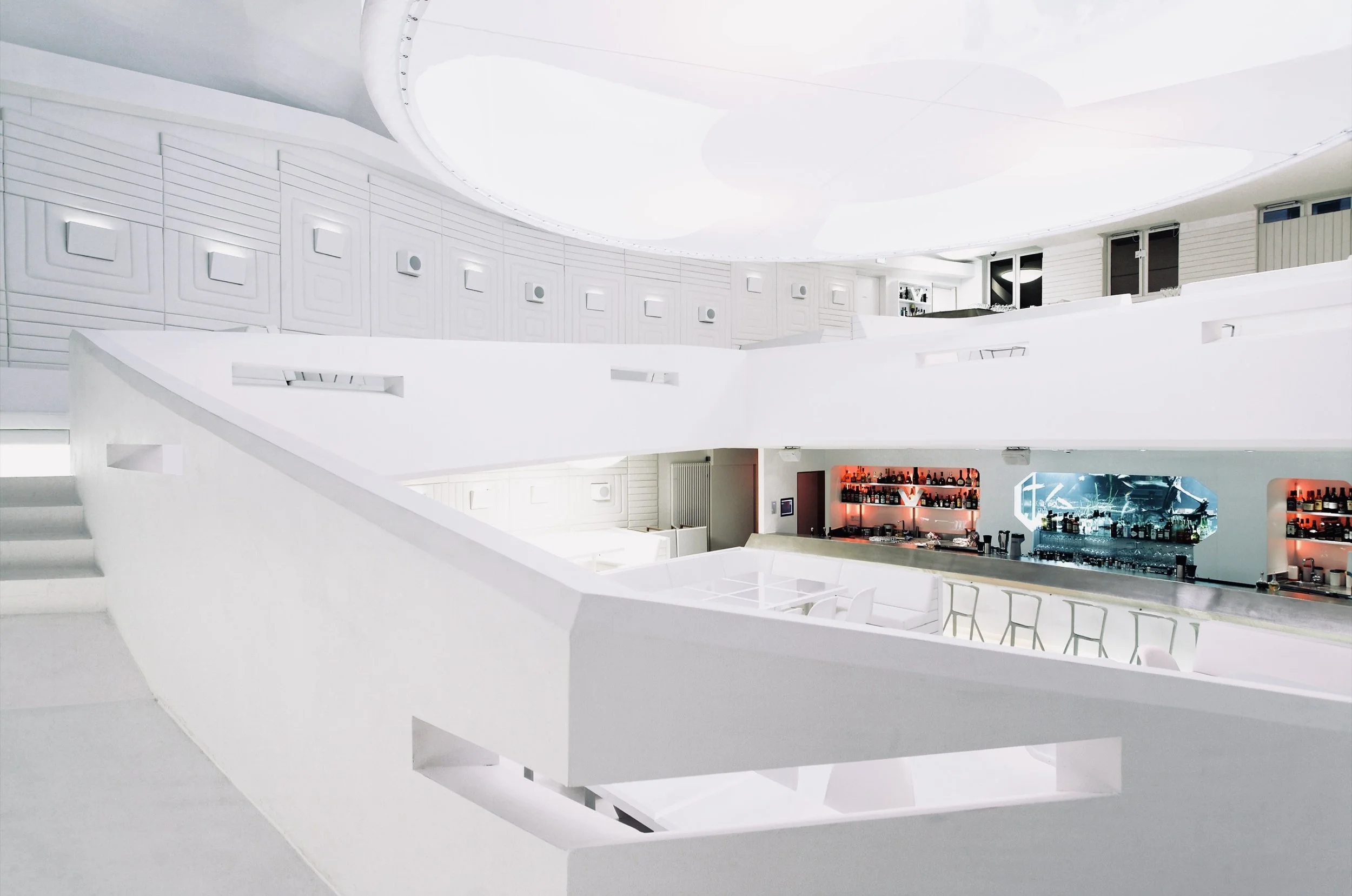 Ein moderner, minimalistischer Barbereich mit weißen Wänden, hoher Decke und integrierten Sitzbereichen.