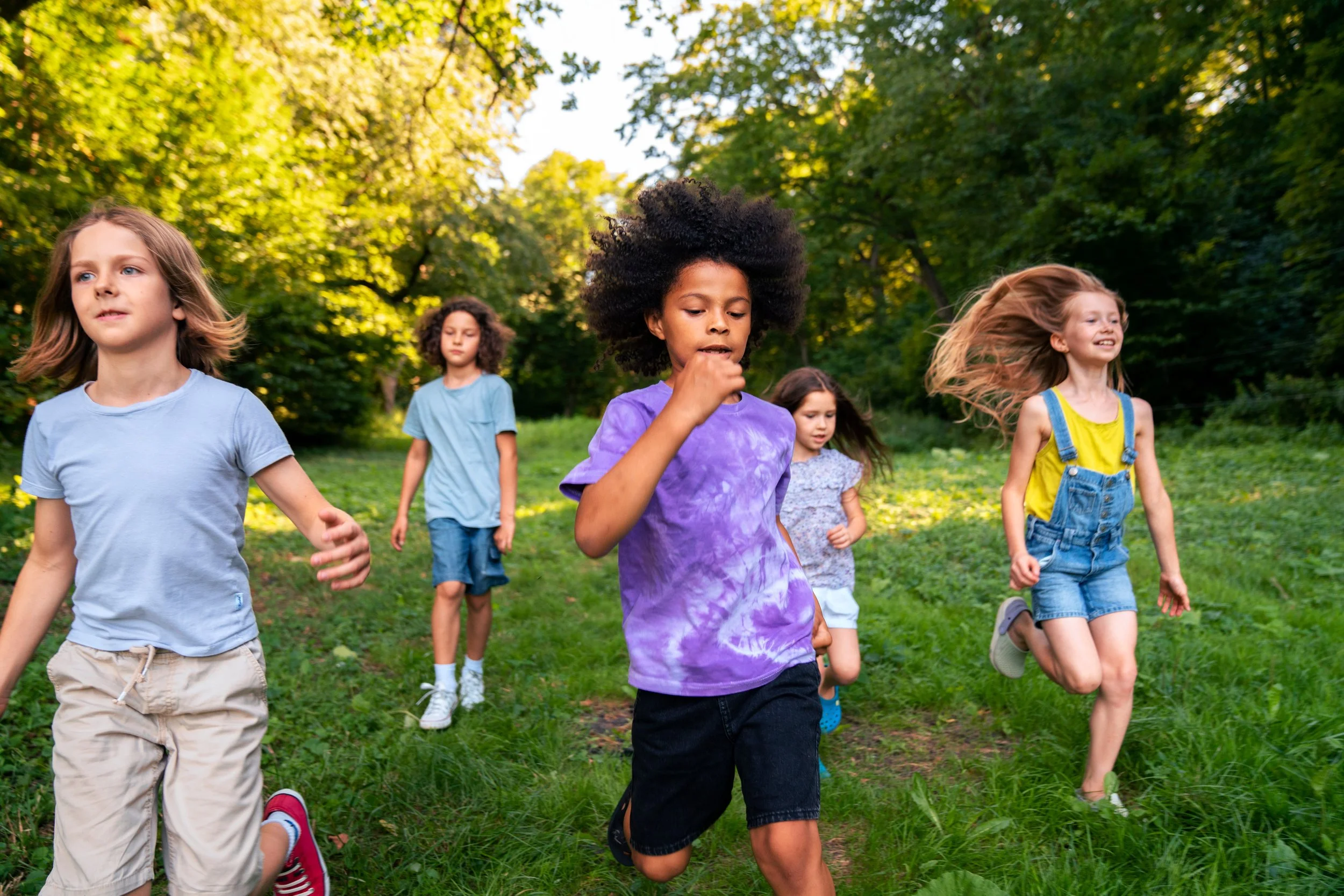 Group of children running through a green park on a sunny day.