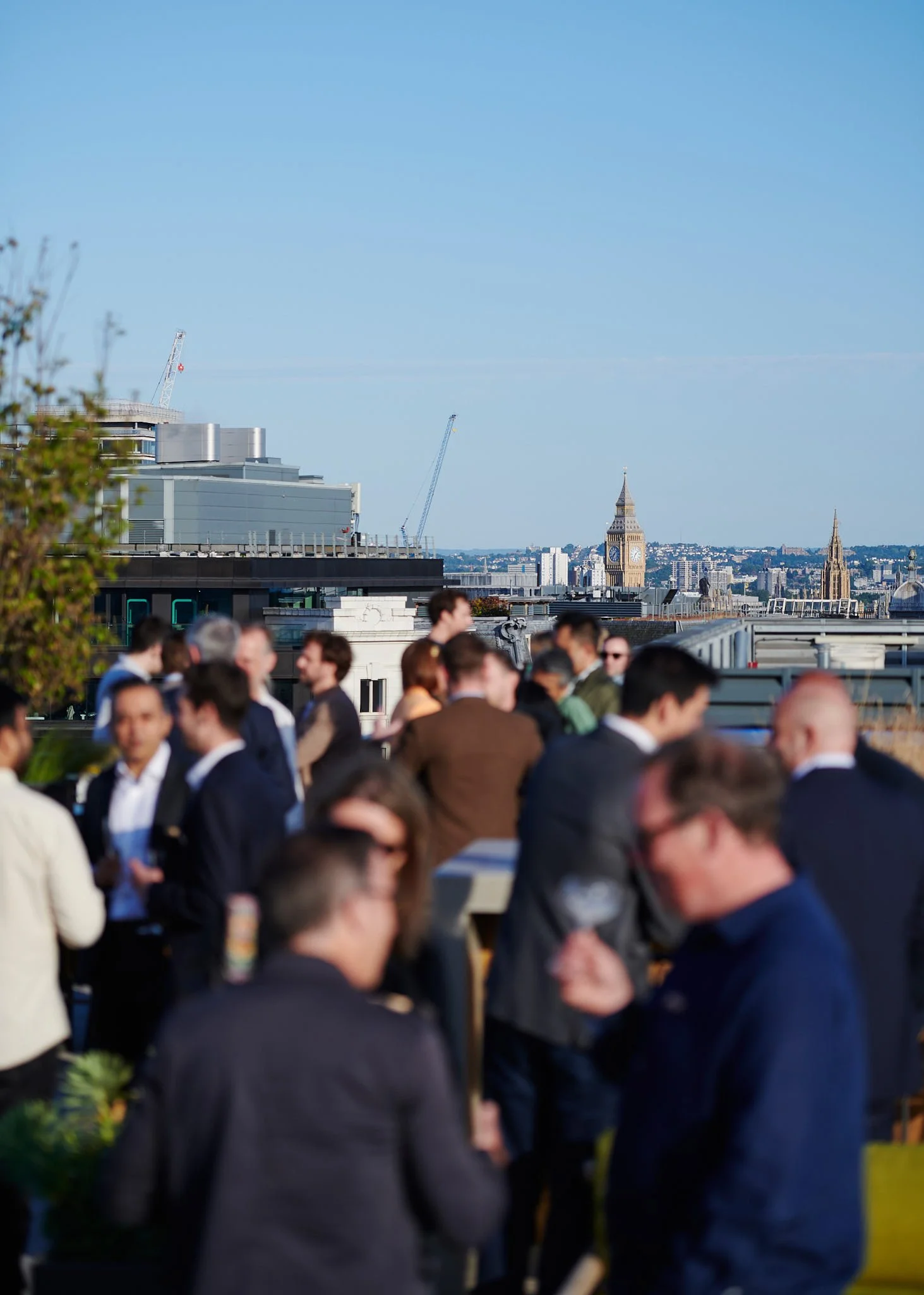 People socializing on a rooftop terrace with a view of London, including Big Ben and other landmarks, on a clear day.