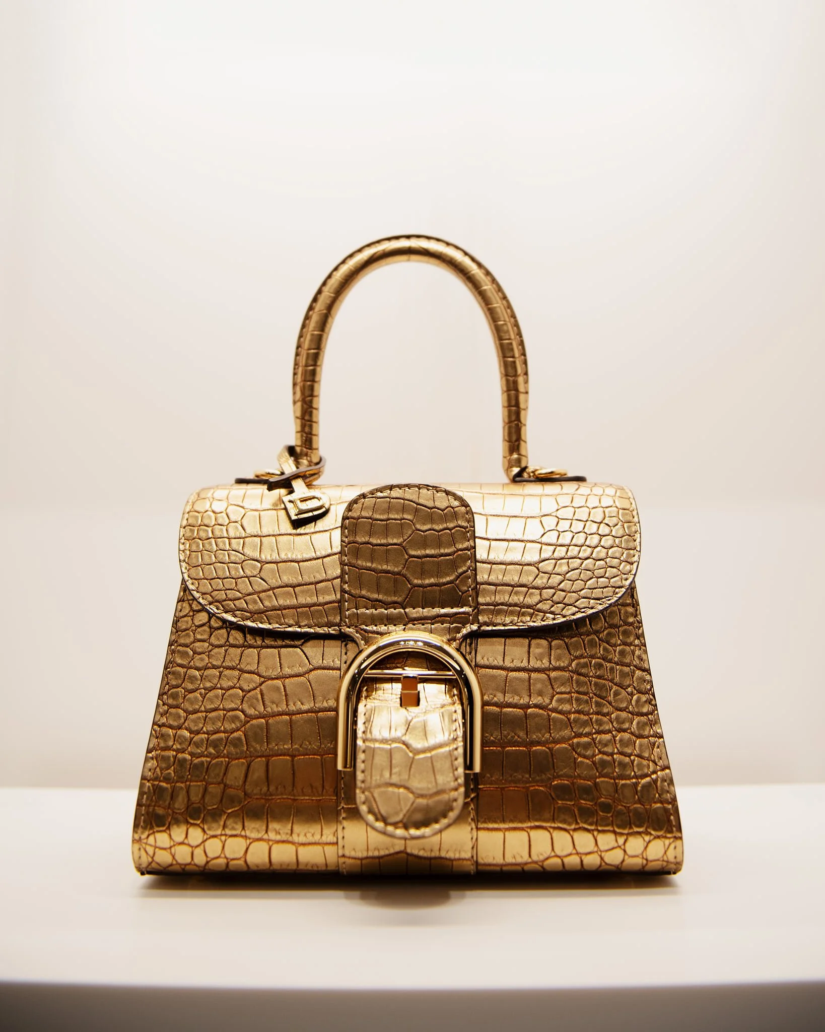 A gold handbag with crocodile texture and a lock detail, displayed against a plain background.