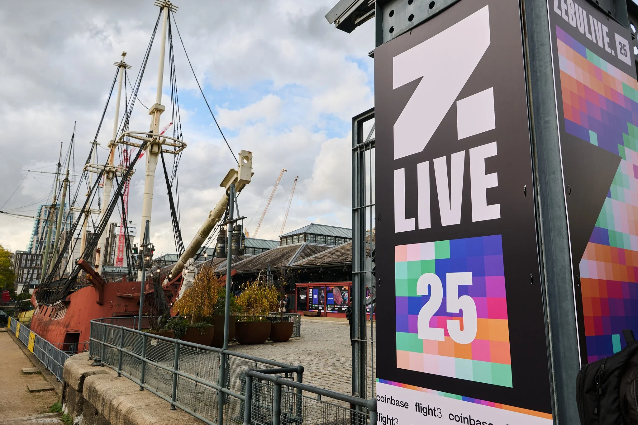 Digital billboard displays the text 'Z Live 25' with a colorful pixelated background near a historic ship at a waterfront event venue under clouded sky.