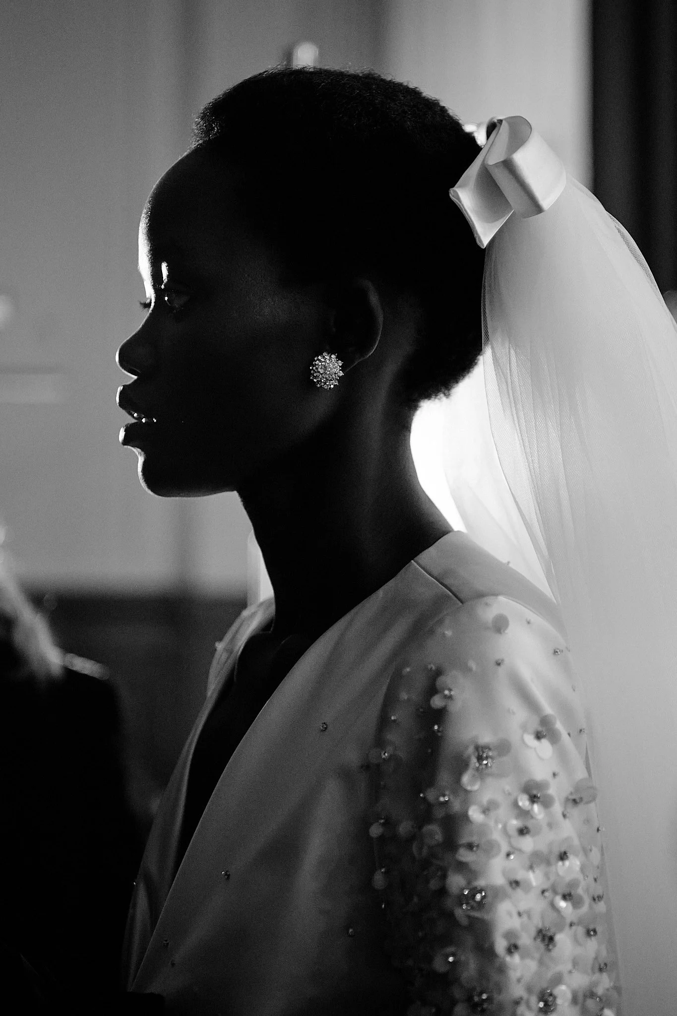 Silhouette of an African American bride with a beaded wedding gown, pearl earrings, and a veil, standing in profile in black and white.