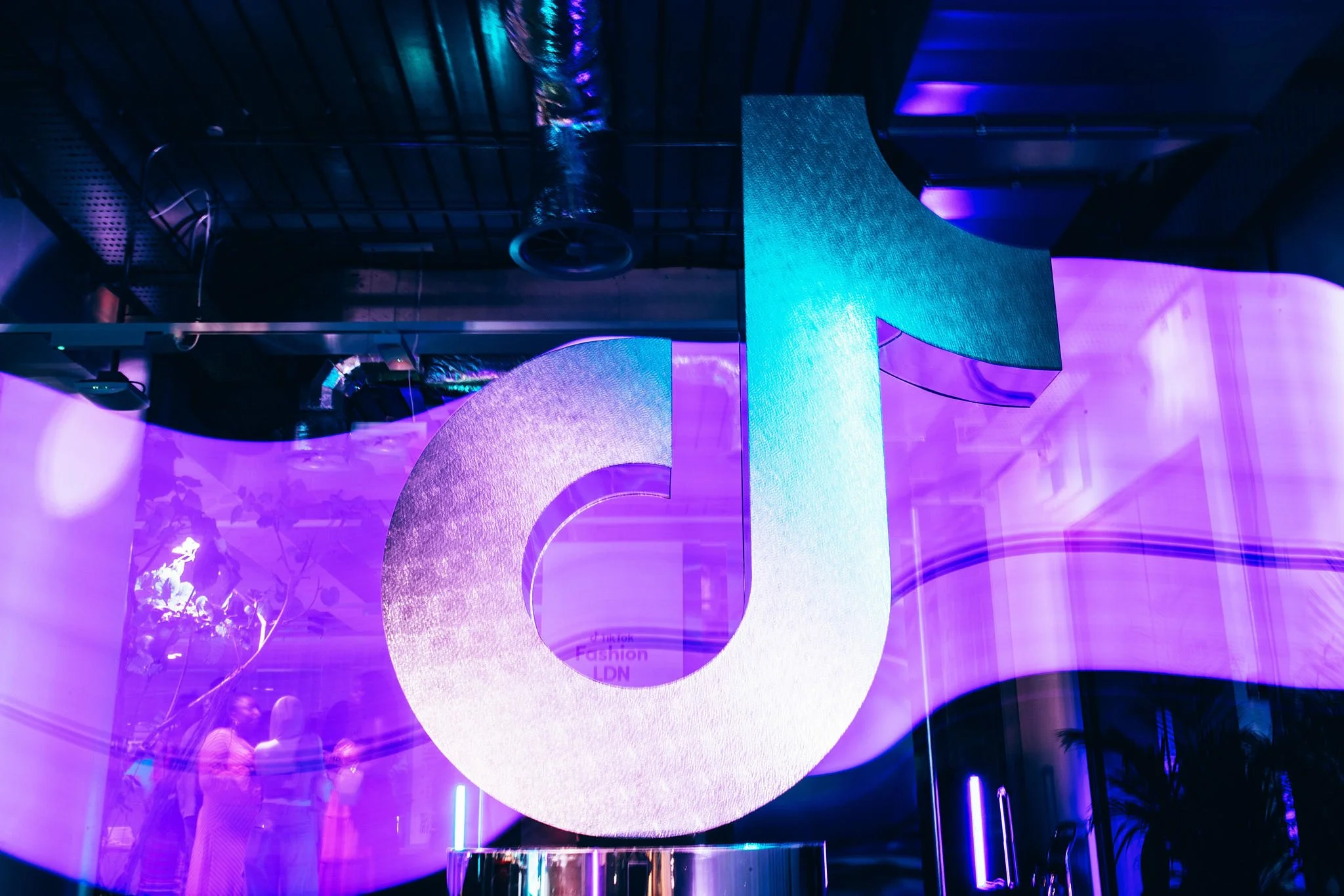 A large, illuminated TikTok logo sculpture in a vibrant purple and blue-lit environment, reflecting a modern, club-like atmosphere.