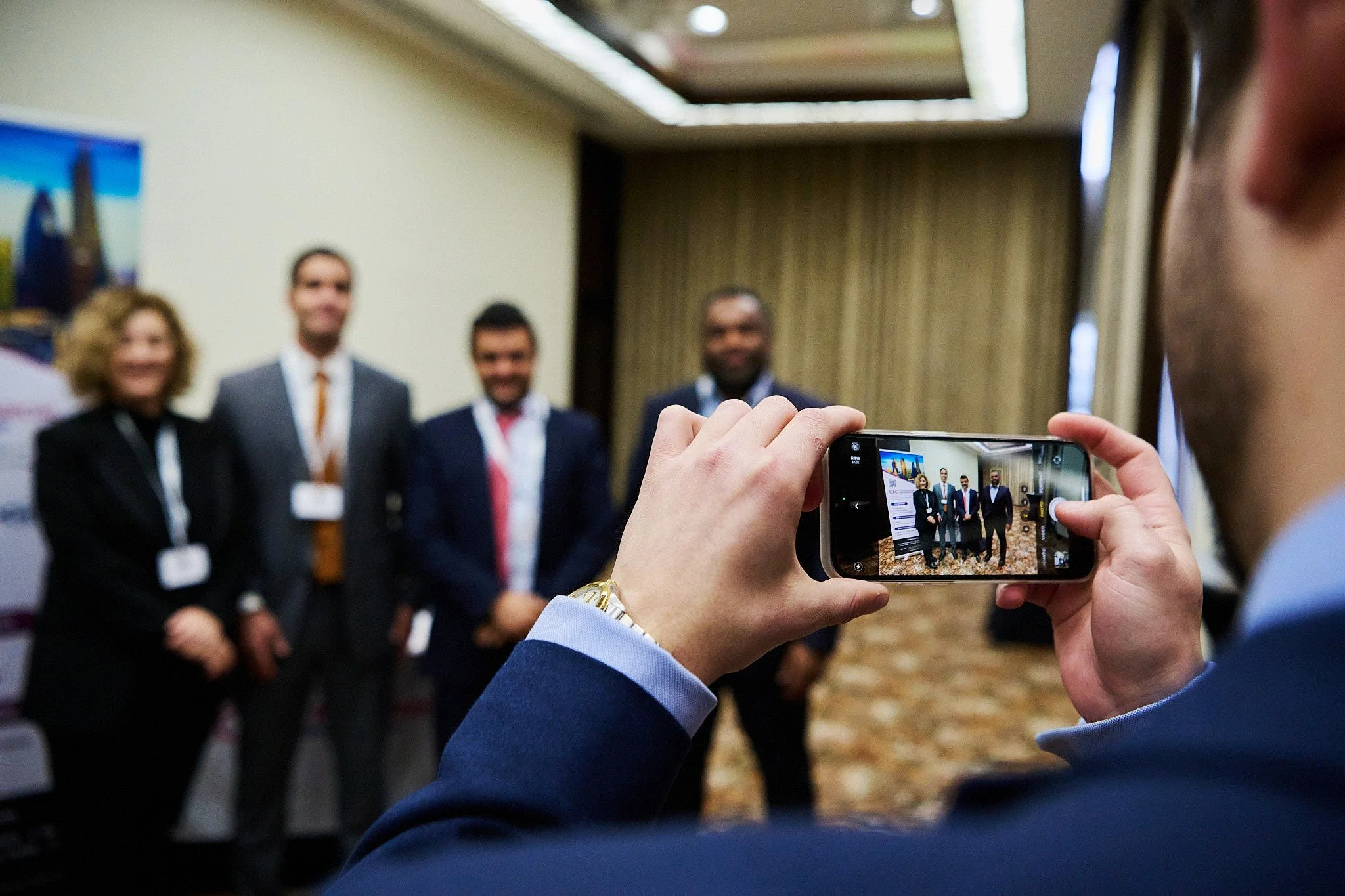 Person taking a photo of a group of four people standing in a line in a conference room.