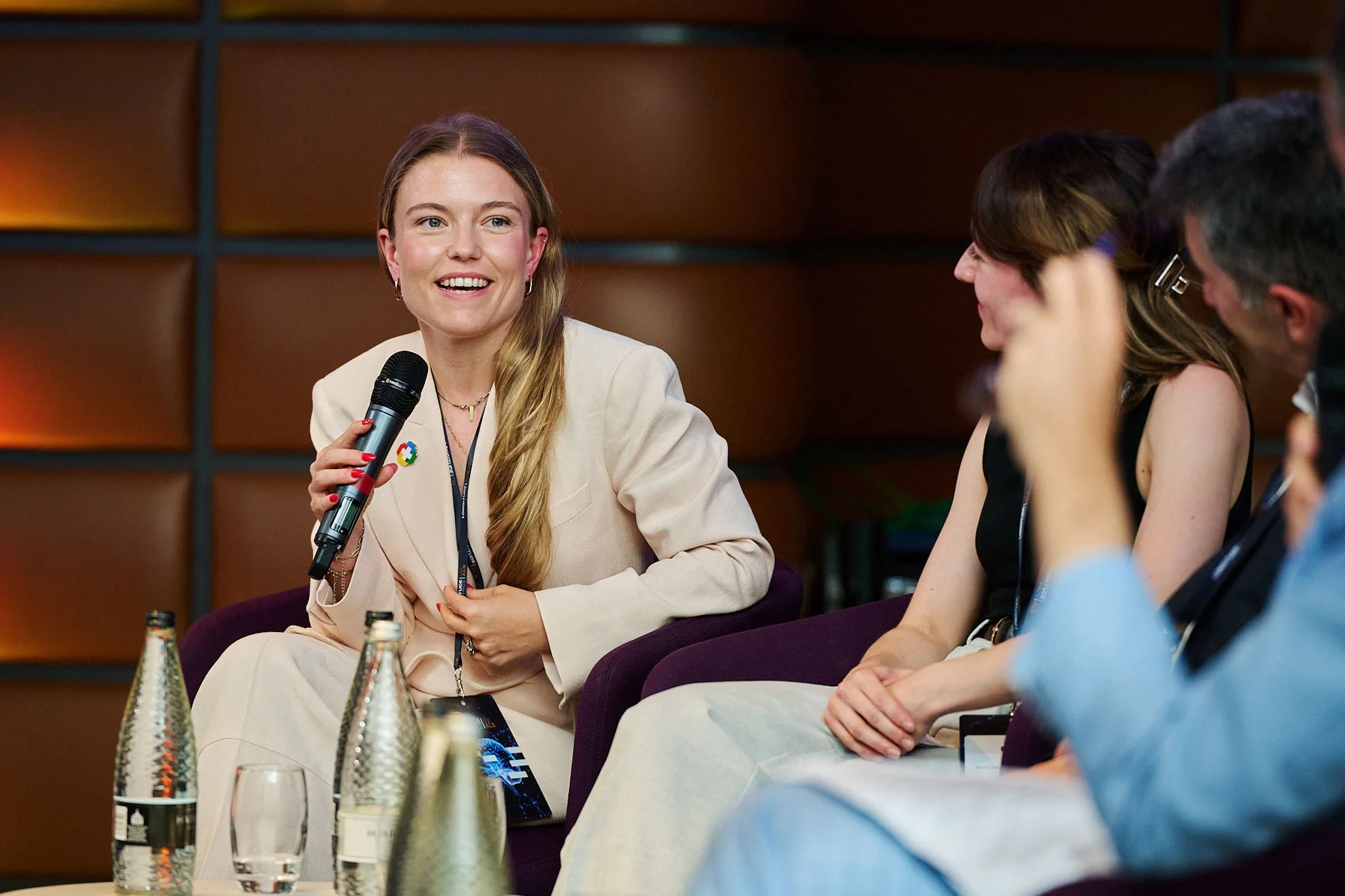 Speaker holding a microphone during a panel discussion at a London corporate event, captured in a natural documentary style.