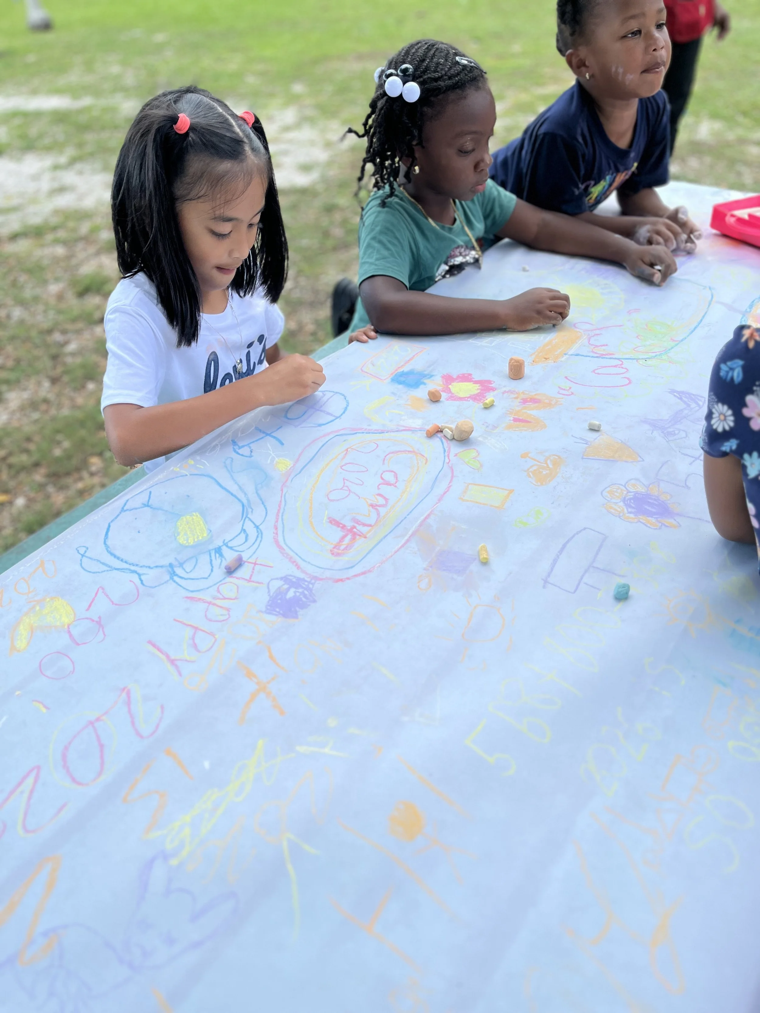 Young children engaged in arts and crafts activities at a classroom table.