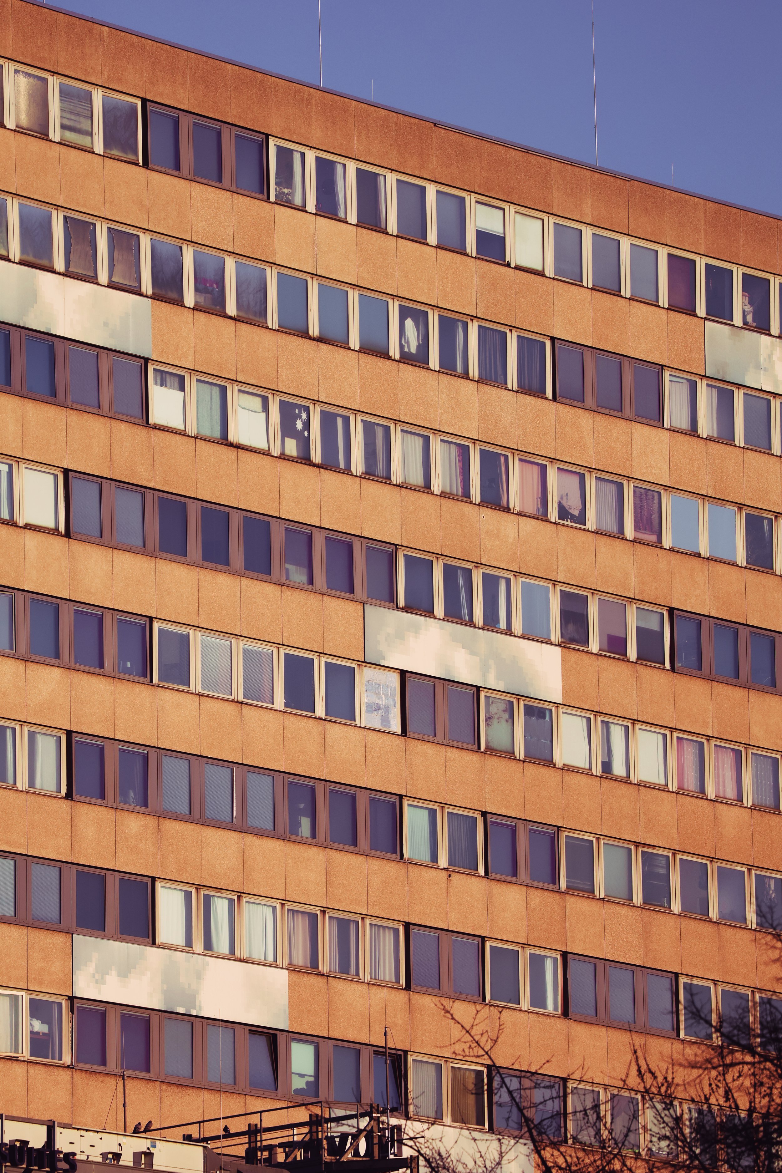 Close-up of a multi-story building with orange brick exterior and many rectangular windows, some reflecting the sky and clouds.