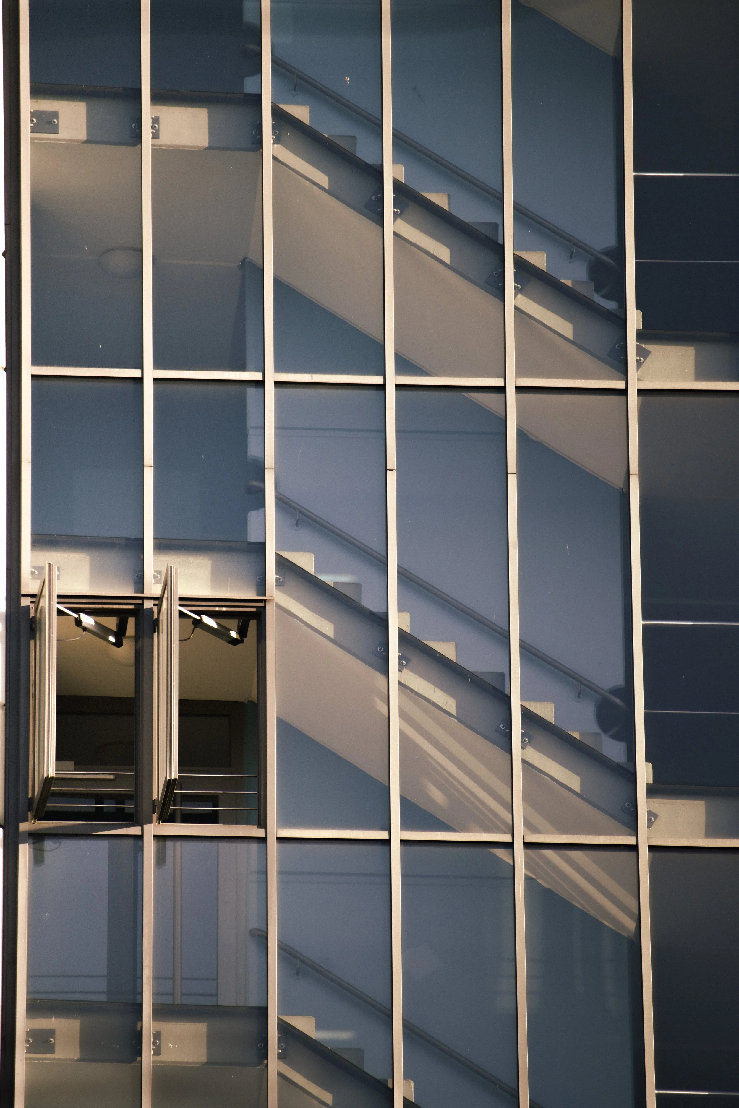 Close-up of a modern glass building with a view of staircases inside, visible through the window panes.