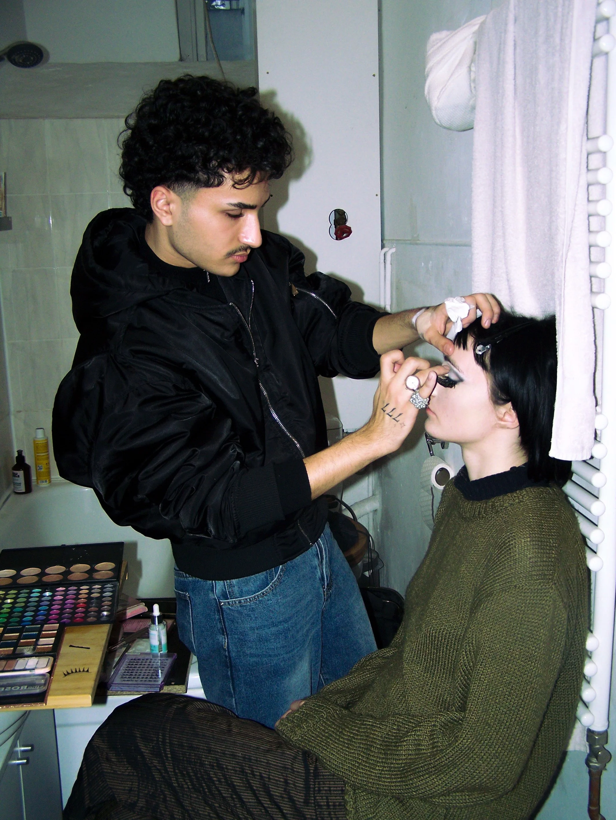 Makeup artist applying eye makeup to a seated woman in a backstage setting.