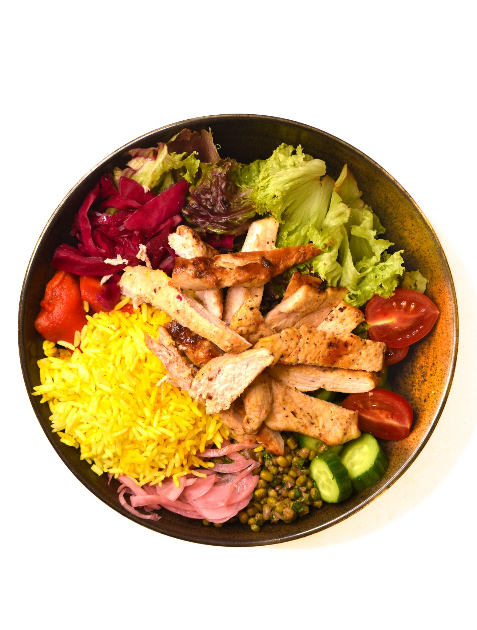 A bowl with mixed greens, cherry tomatoes, sliced cucumbers, grilled chicken strips, yellow rice, pickled red onions, peas, shredded red cabbage, and tortilla strips.