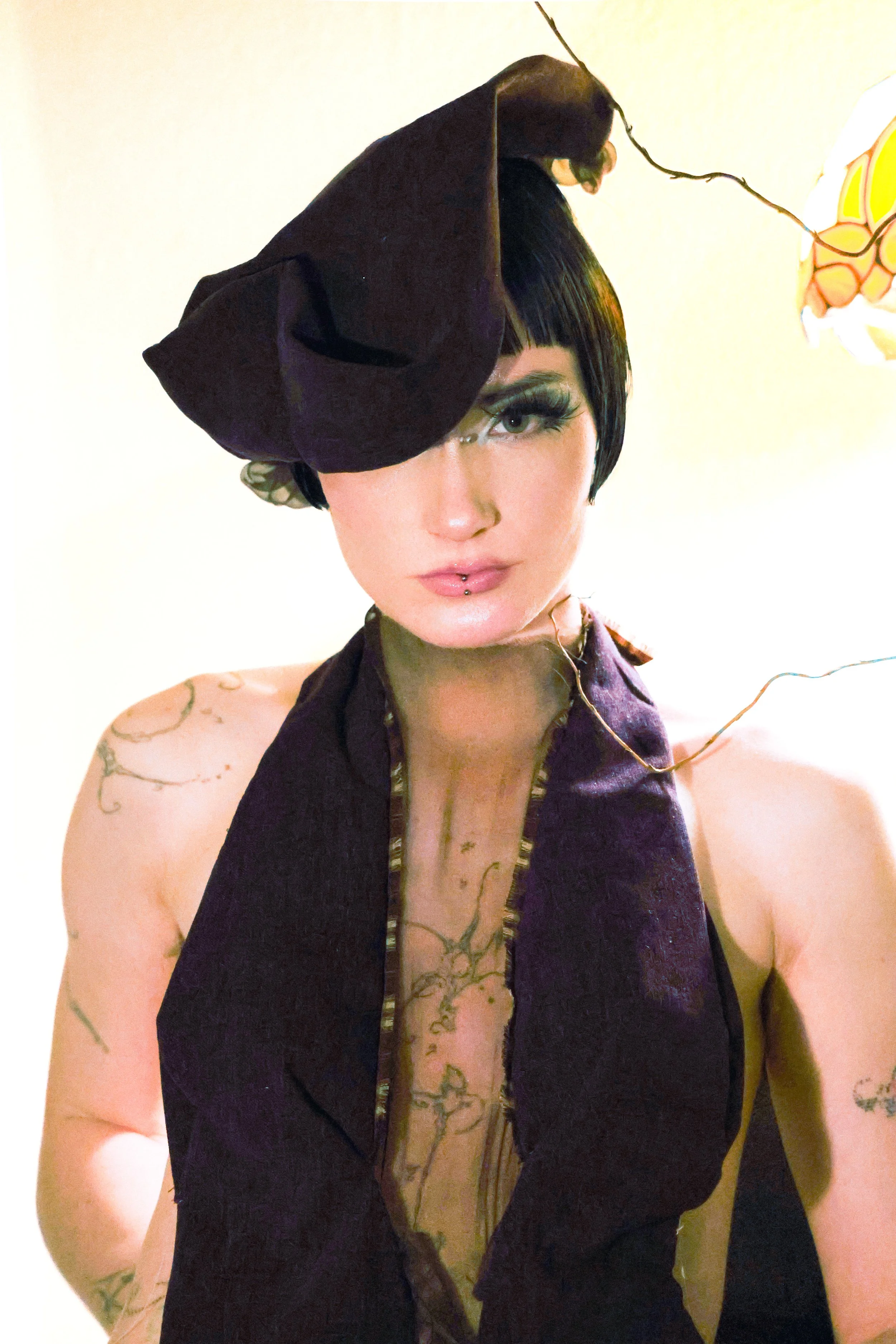 A woman with short black hair and tattoos wearing a dark purple headpiece and a matching open jacket.