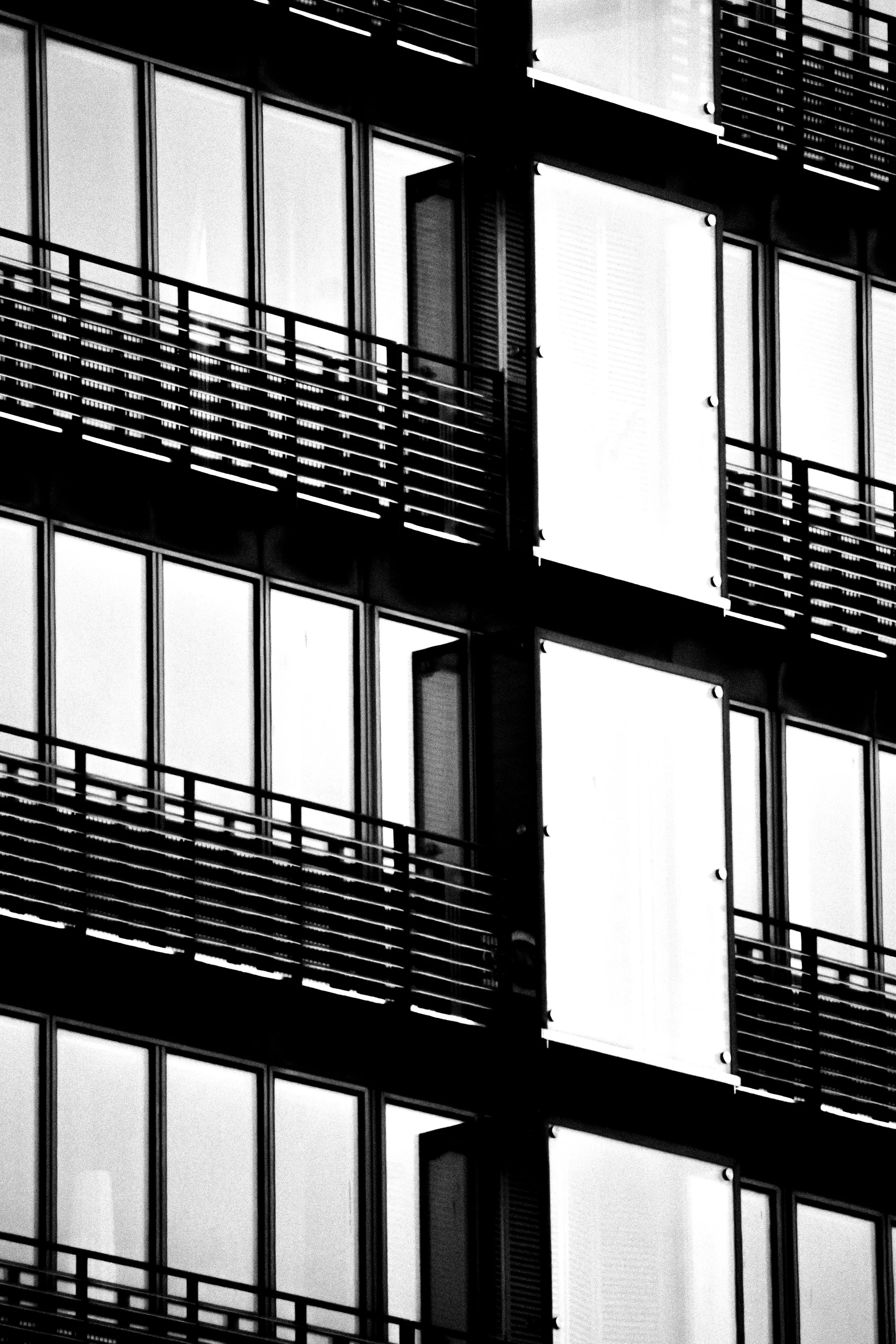 Black and white close-up of a modern building's facade with multiple windows, balconies with horizontal railings, and visible exterior panels.