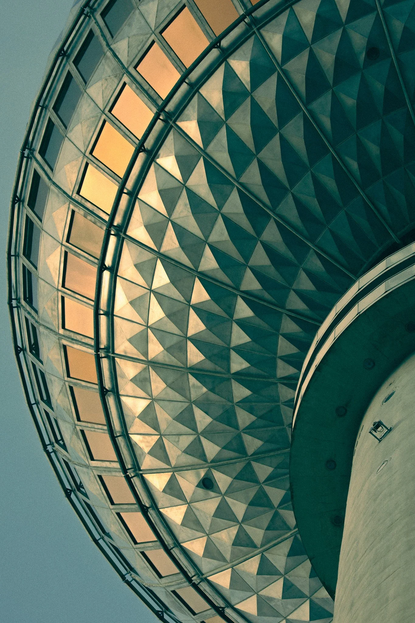 Low-angle view of a modern, curved building with a geometrically patterned facade and illuminated windows.