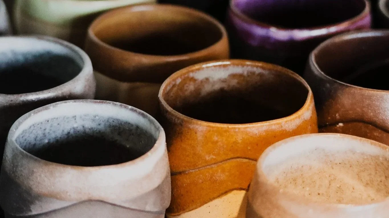 Various ceramic cups filled with dark beverages, arranged closely together.