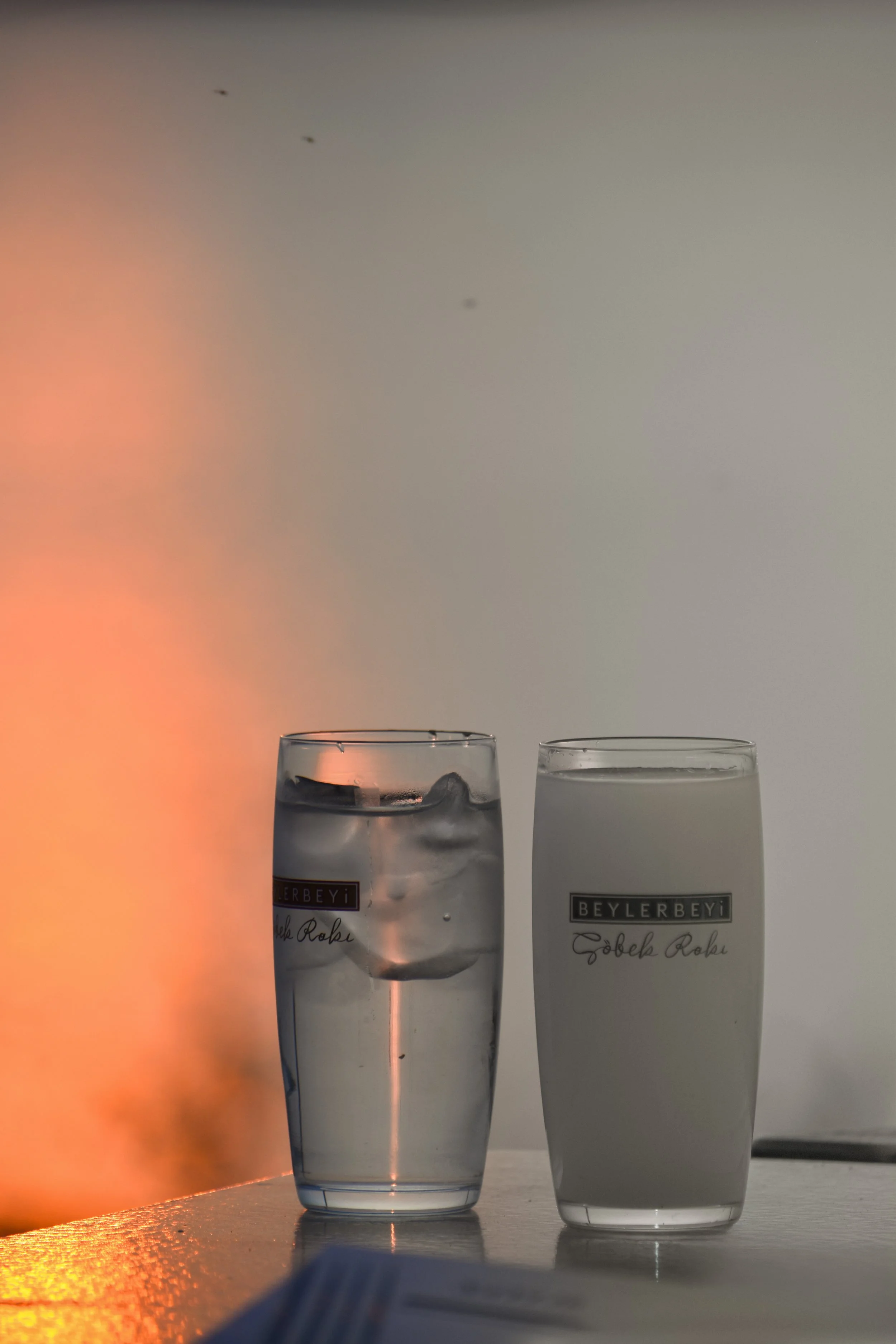 Two glasses, one filled with water and ice and the other with milk, placed on a table against a plain background.