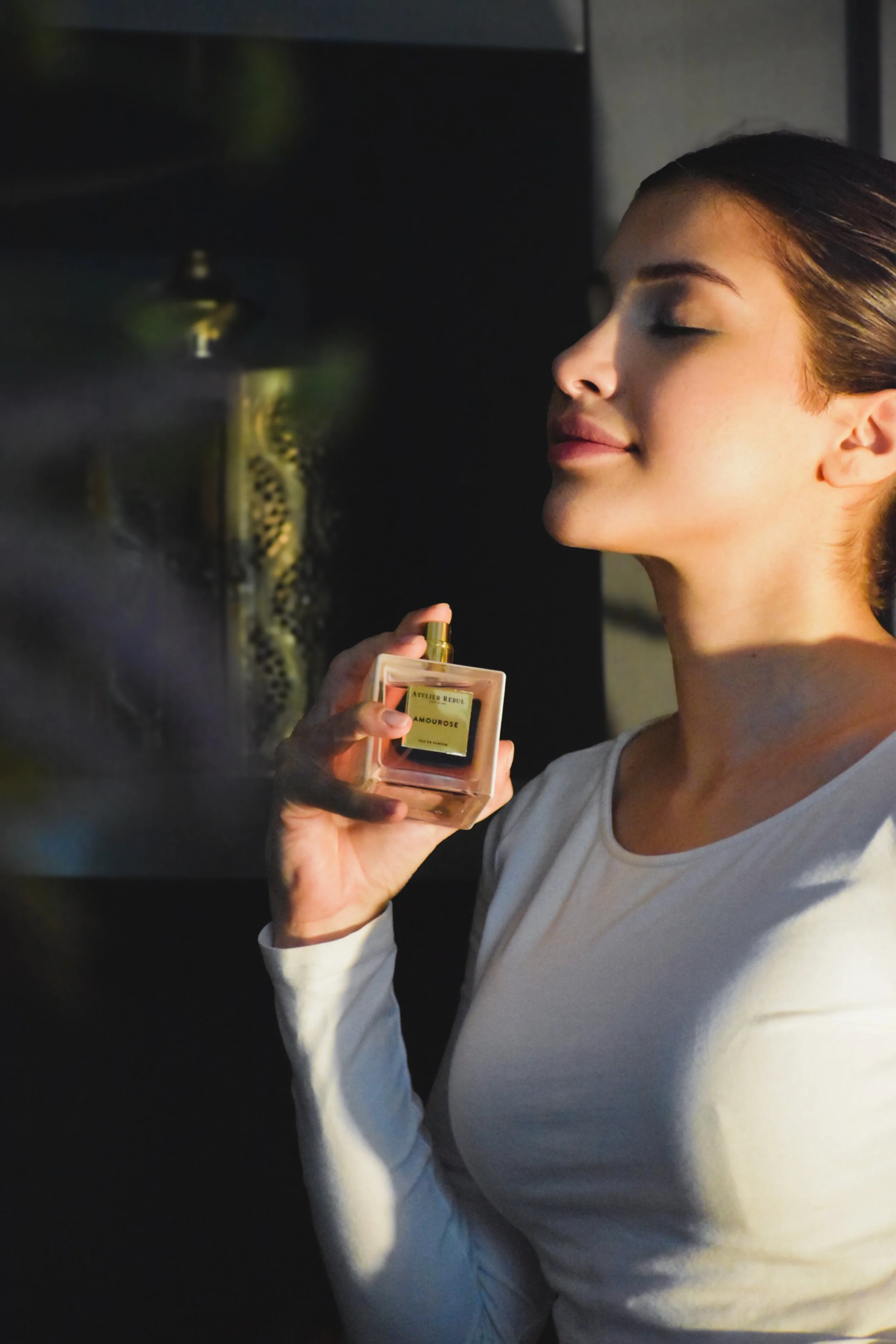A woman with closed eyes holding a perfume bottle near her face, enjoying the fragrance.