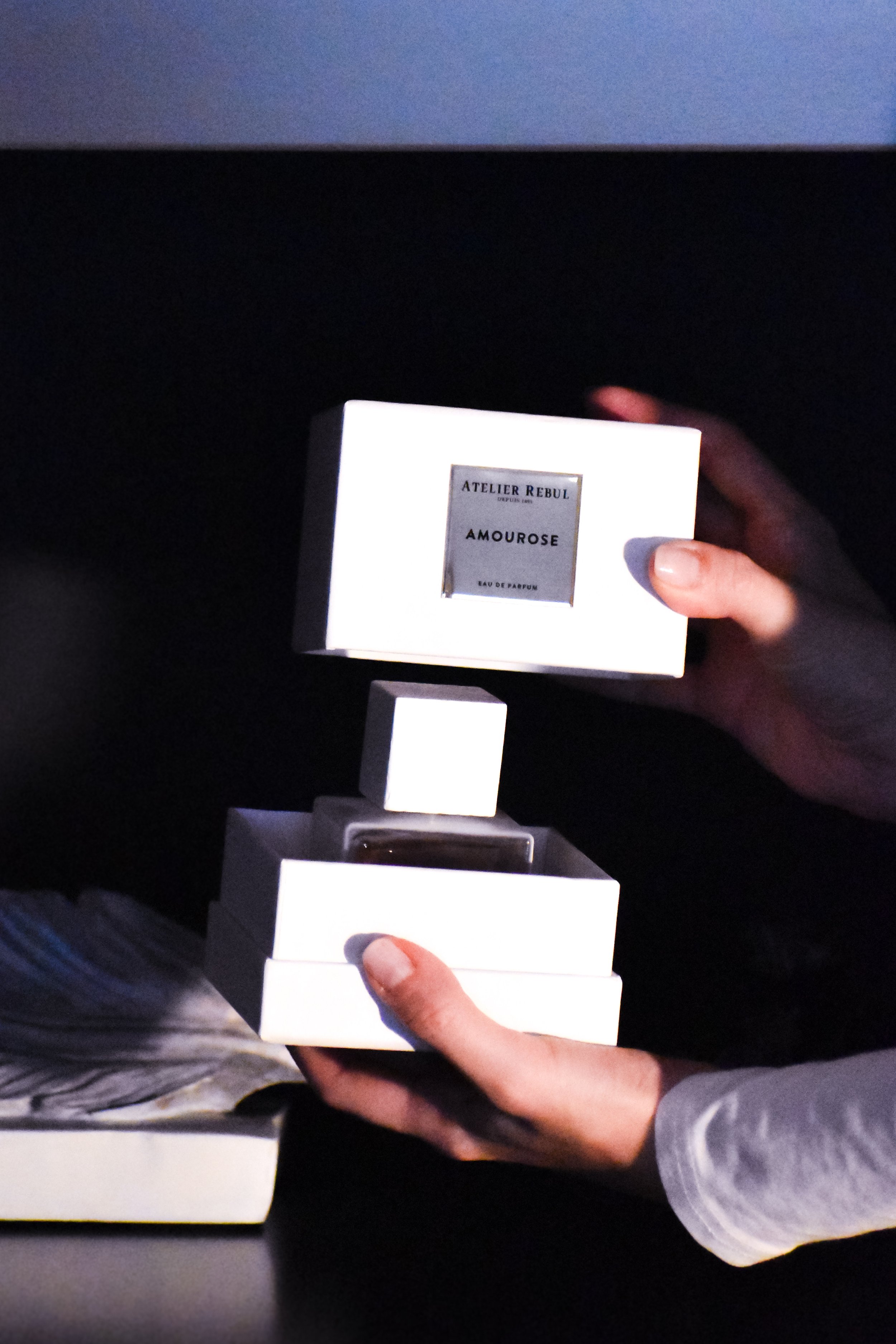 Person holding a white box with a perfume bottle inside, labeled 'Atelier Rebul Amouroze Eau de Parfum.'