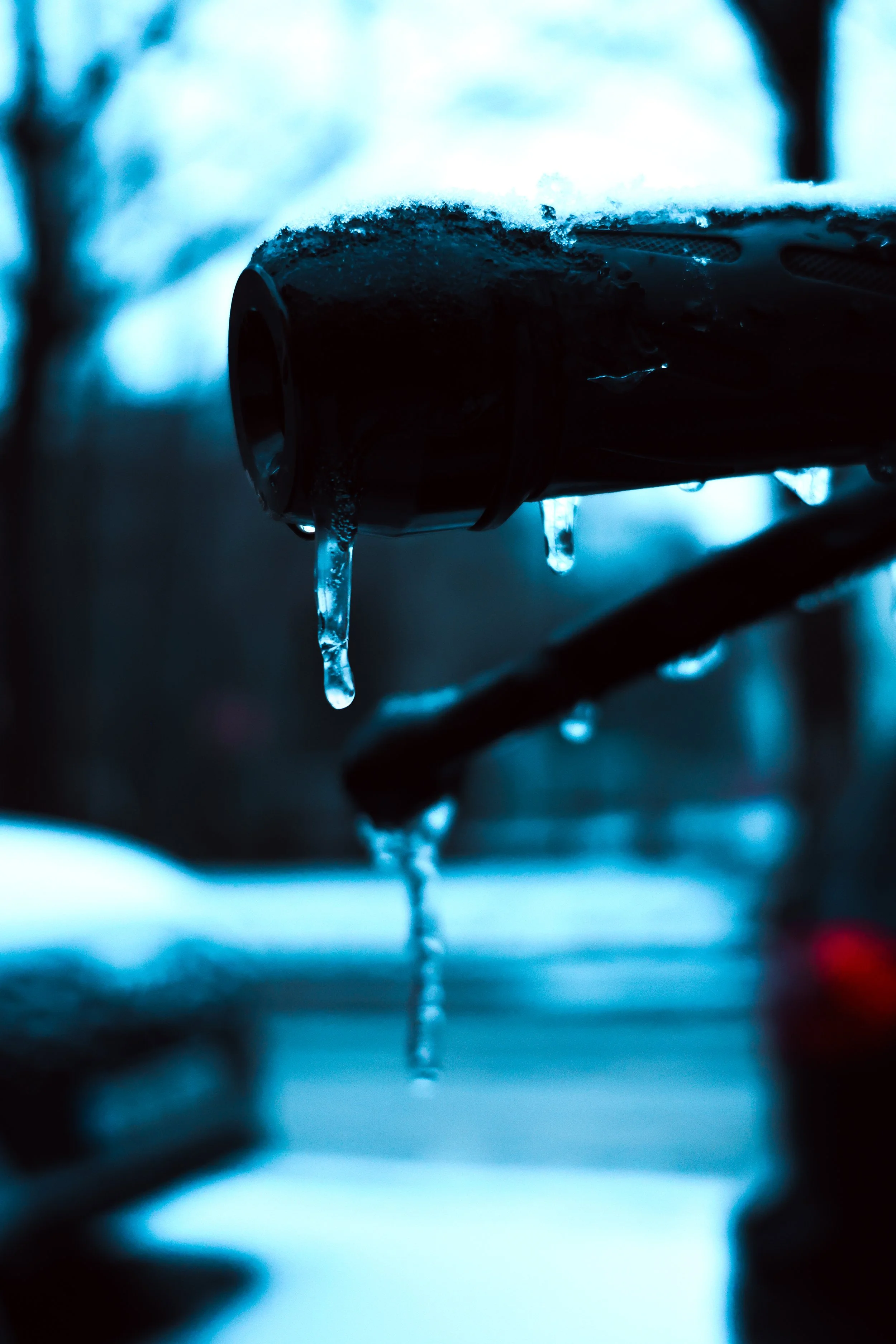 Close-up of a bike handlebar with ice and water droplets hanging from it during winter.