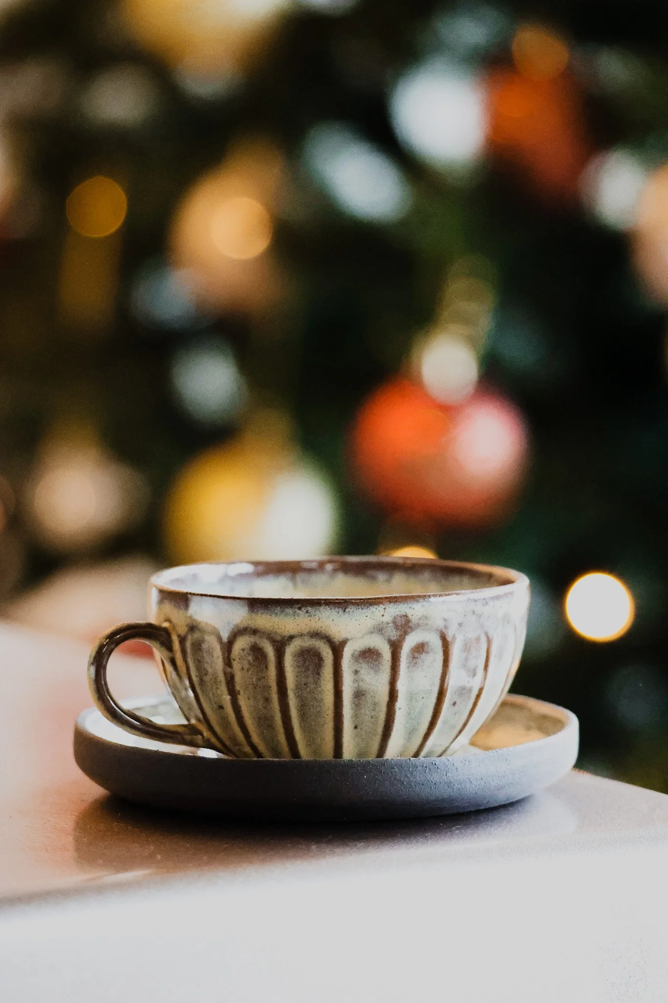 A ceramic teacup with a matching saucer on a table, with a blurred Christmas tree in the background