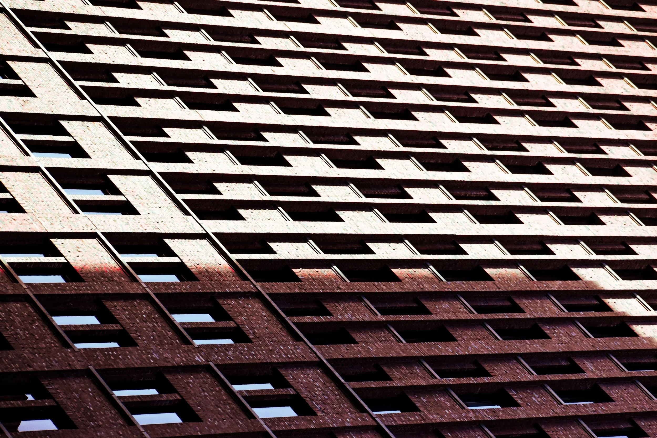 Close-up view of a tall brick building with multiple rows of windows, slightly tilted angle.