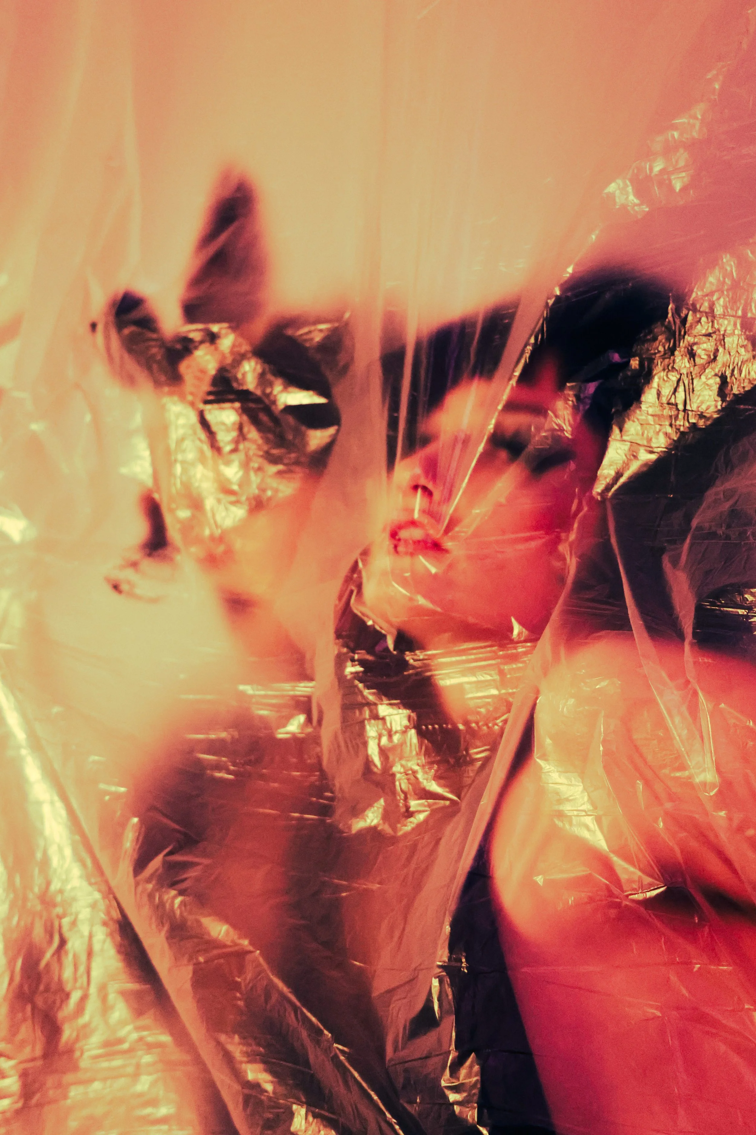 Close-up of crumpled metallic foil with warm orange and red tones, reflecting light and creating abstract shapes.