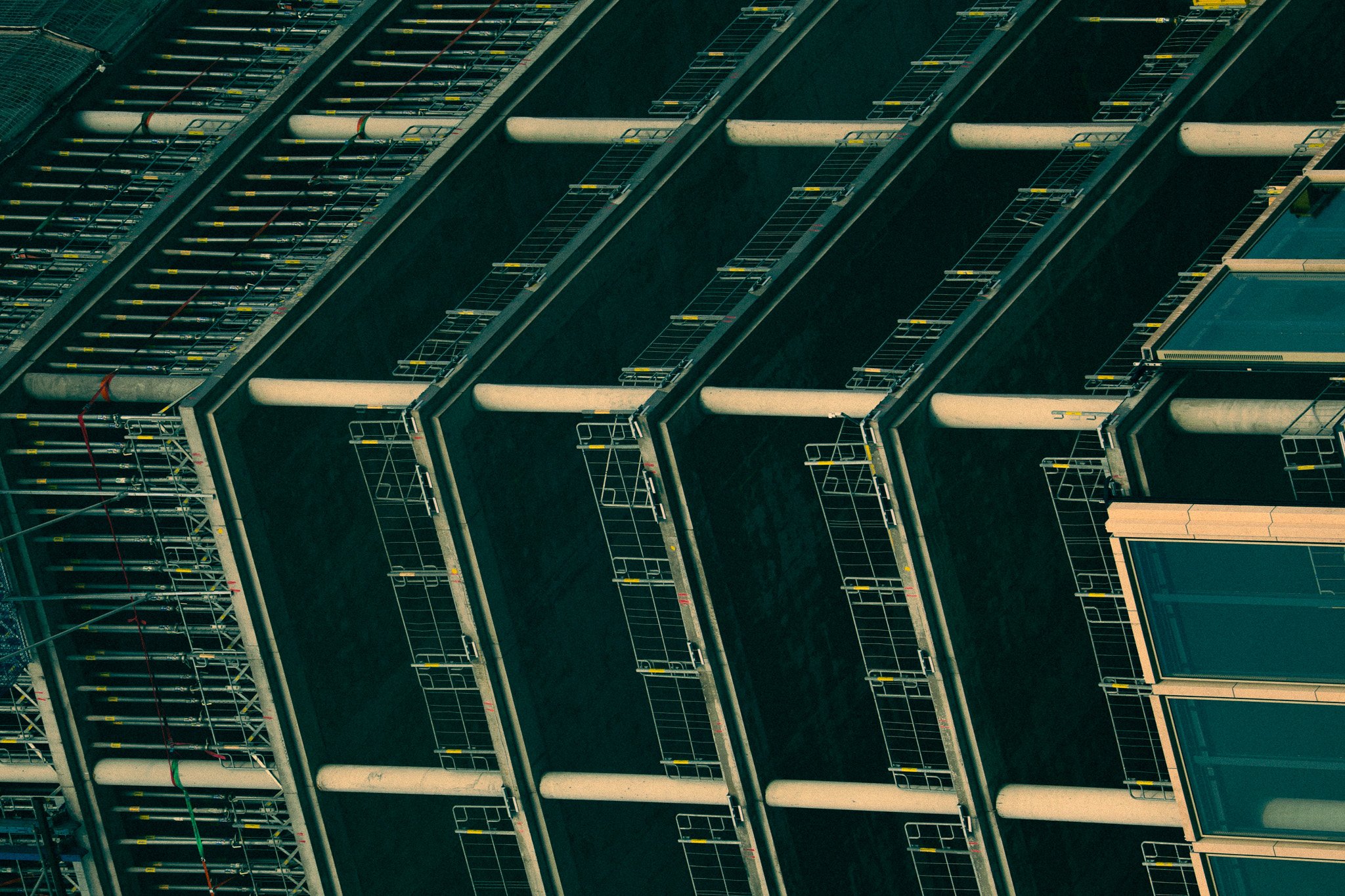 Close-up of a modern building's exterior with multiple balconies featuring metal railings, pipes, and glass windows.