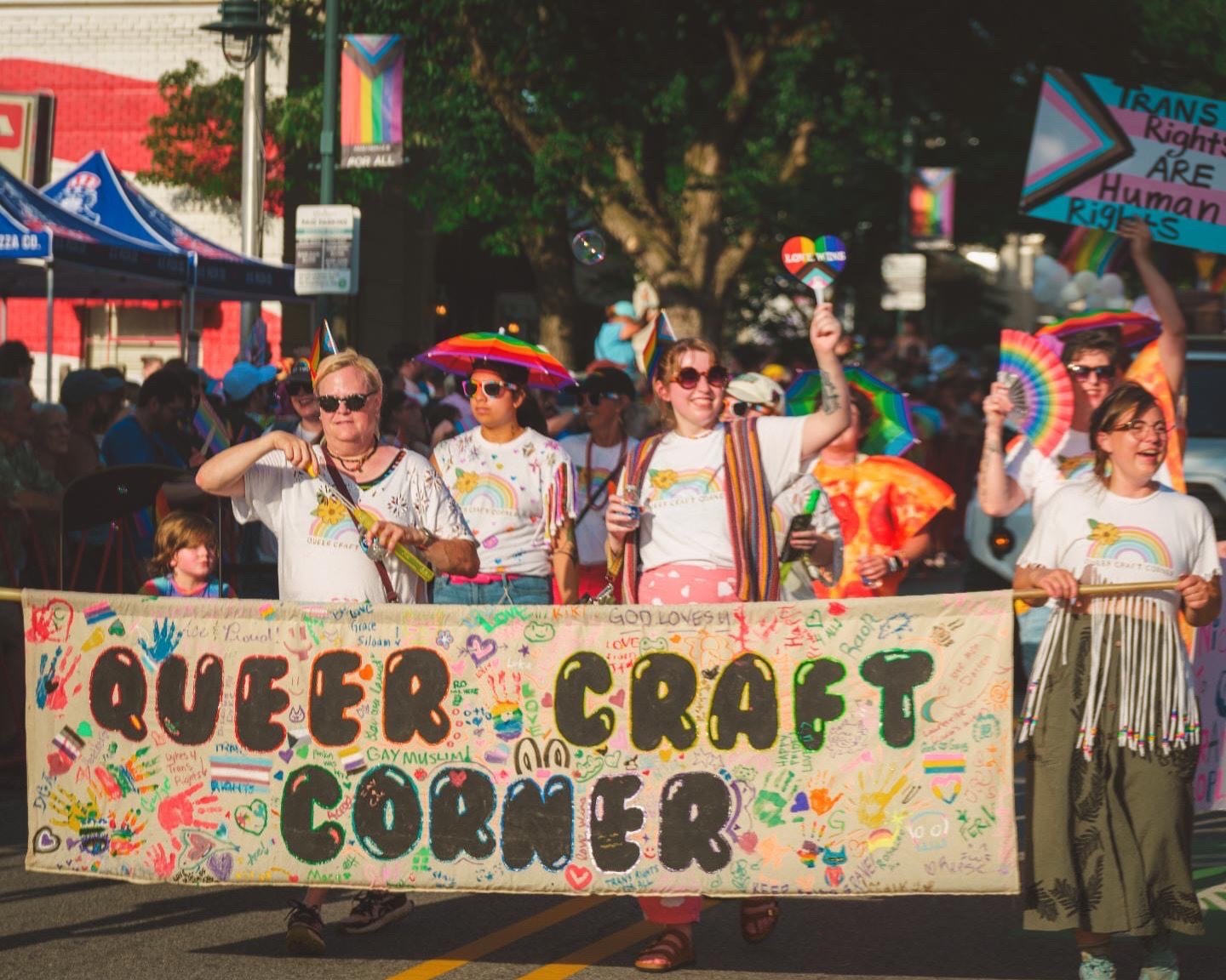 A huge thank you to our friend along the Pride parade route for capturing this beautiful photo of the Queer Craft Corner team and our community-made banner. 💖

This banner was created by so many hands at our booth. Thank you to everyone who painted,