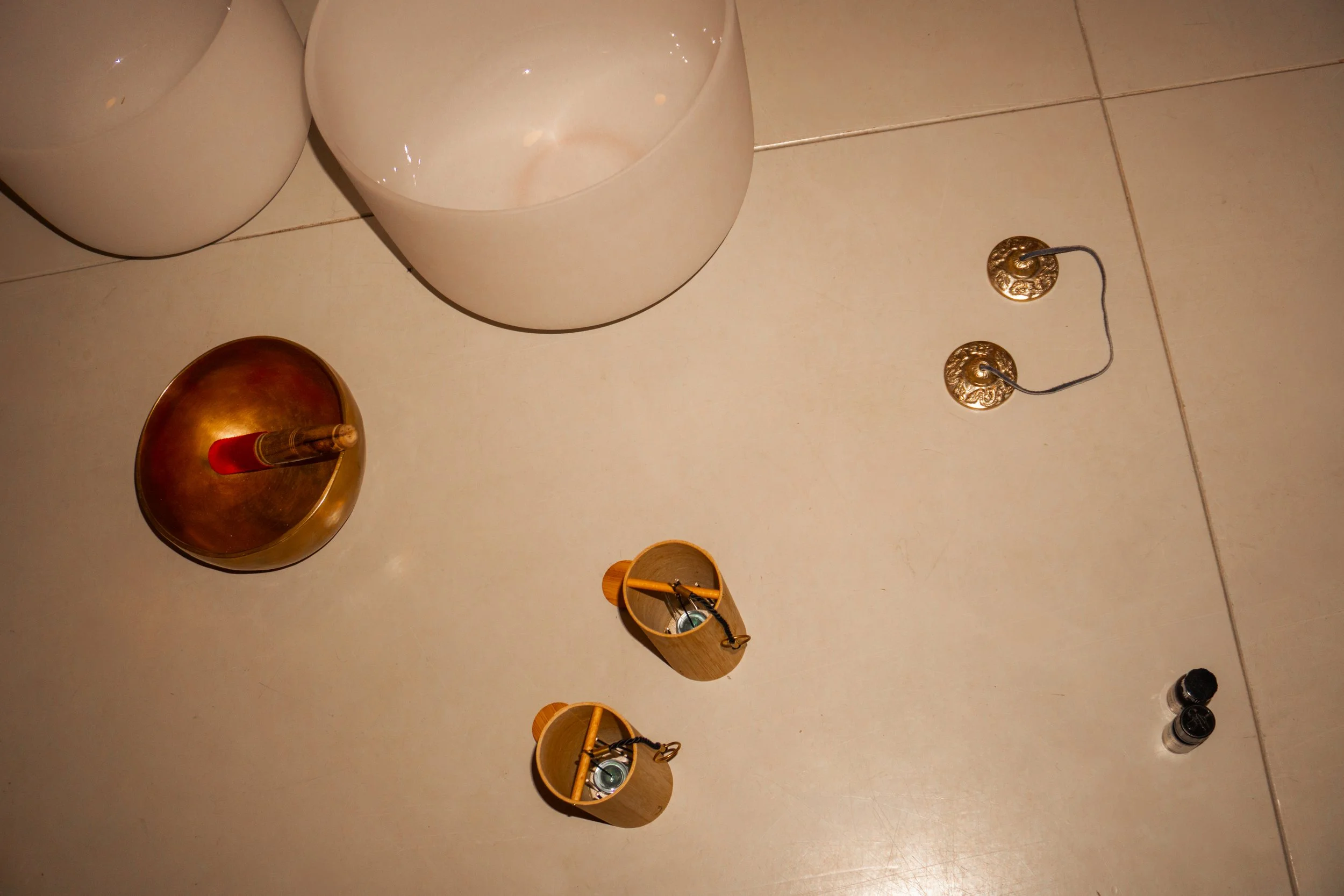 Decorative objects on a floor, including beige and white crystal bowls, a Koshi chime, a brass singing bowl, and a tingsha bell.