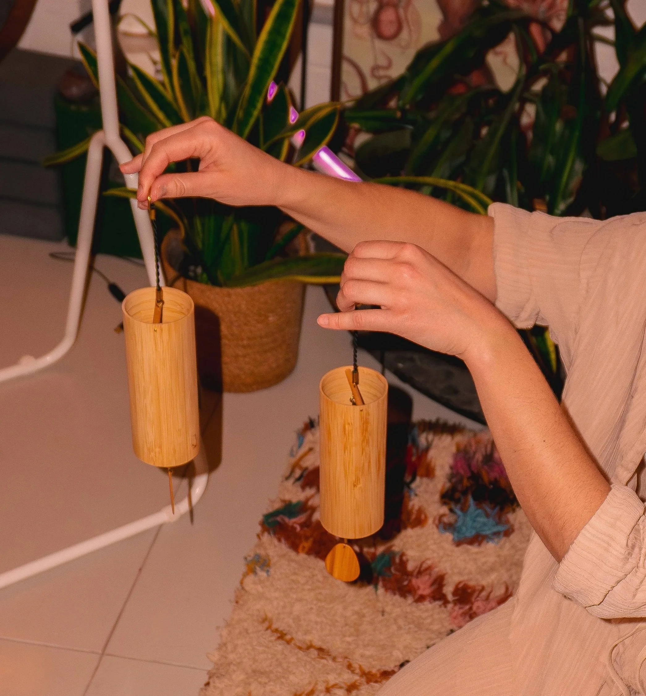 A person is playing bamboo Koshi wind chimes, with large green leafy plants in the background.