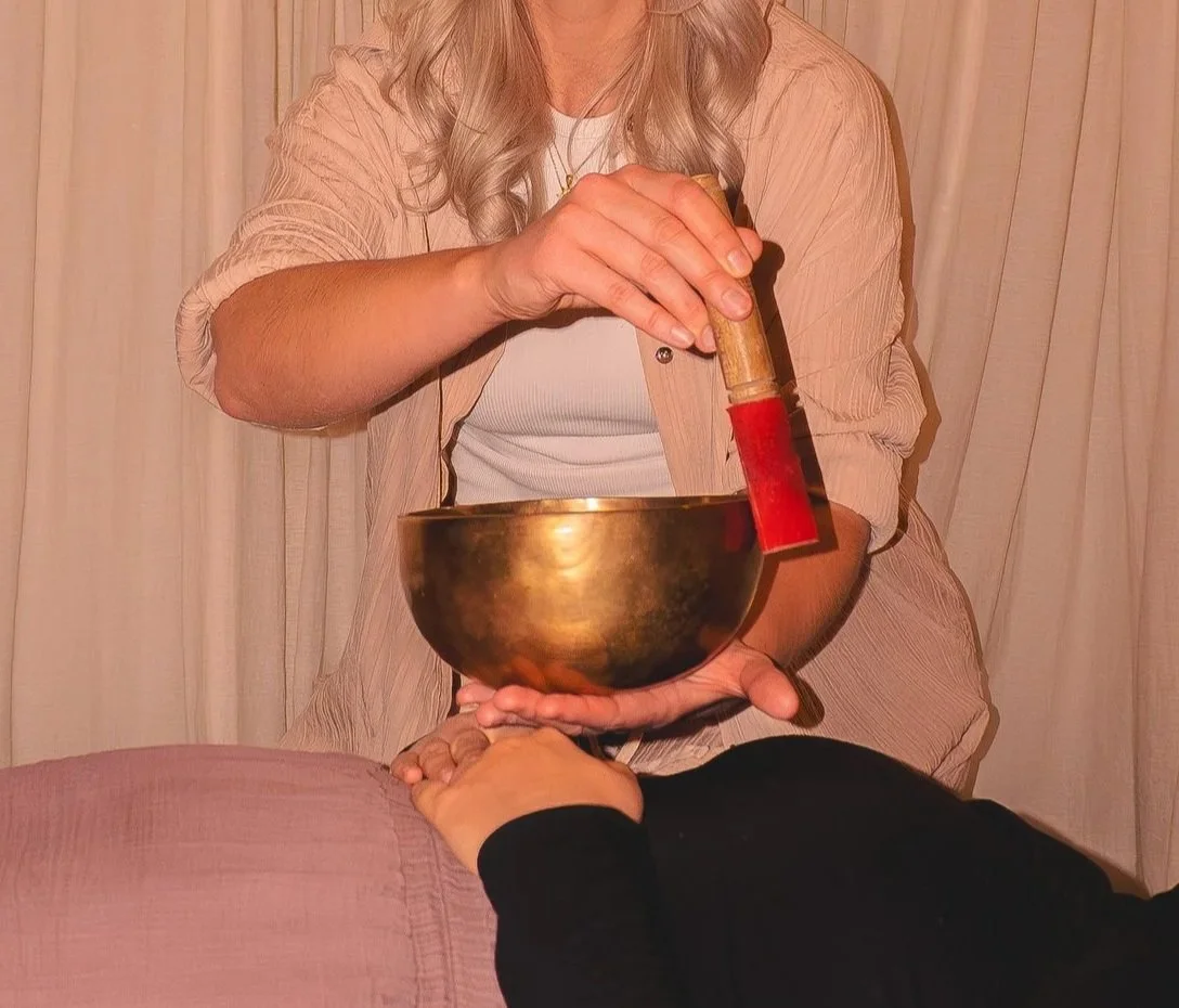 A woman sitting down appears to be holding a large himalayan singing bowl. She's singing the bowl with a wooden mallet with red suede on the end.