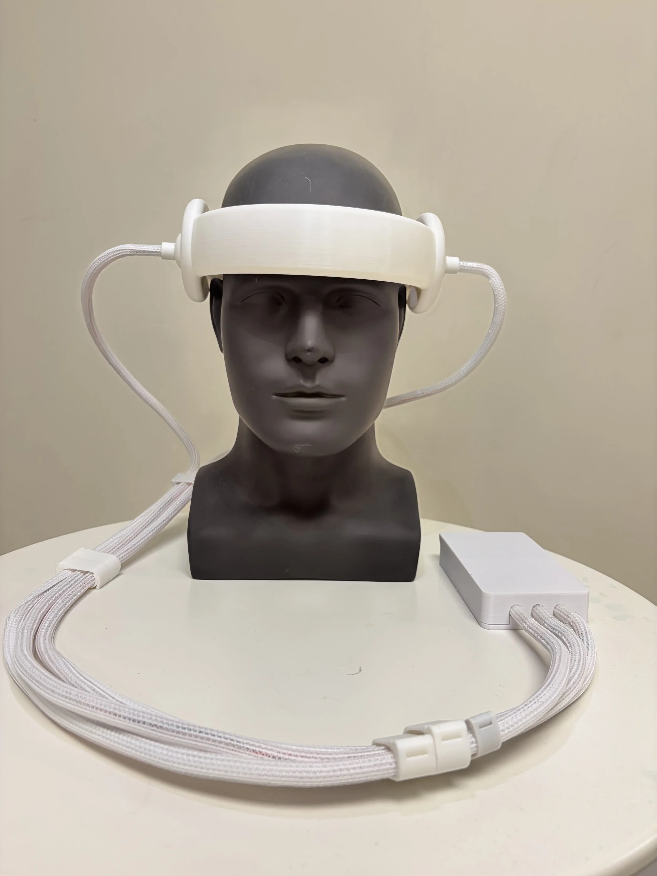 Headset connected to a black mannequin head with a white headband and cable, placed on a white surface.