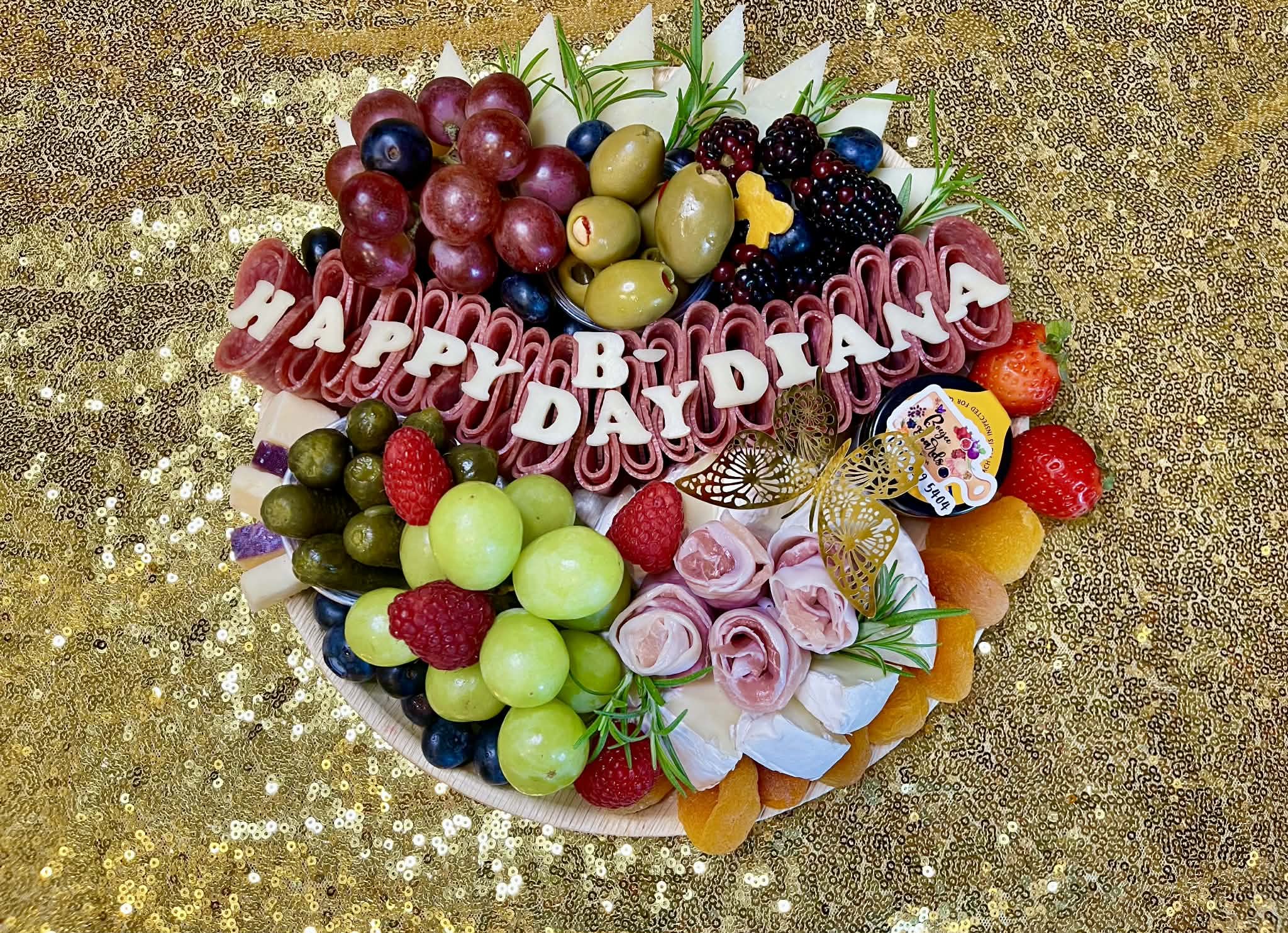 Happy birthday theme charcuterie board featuring assorted meats, cheeses and fresh fruit including green and purple grapes, green olives and cheese letters cut out to say happy bday diana