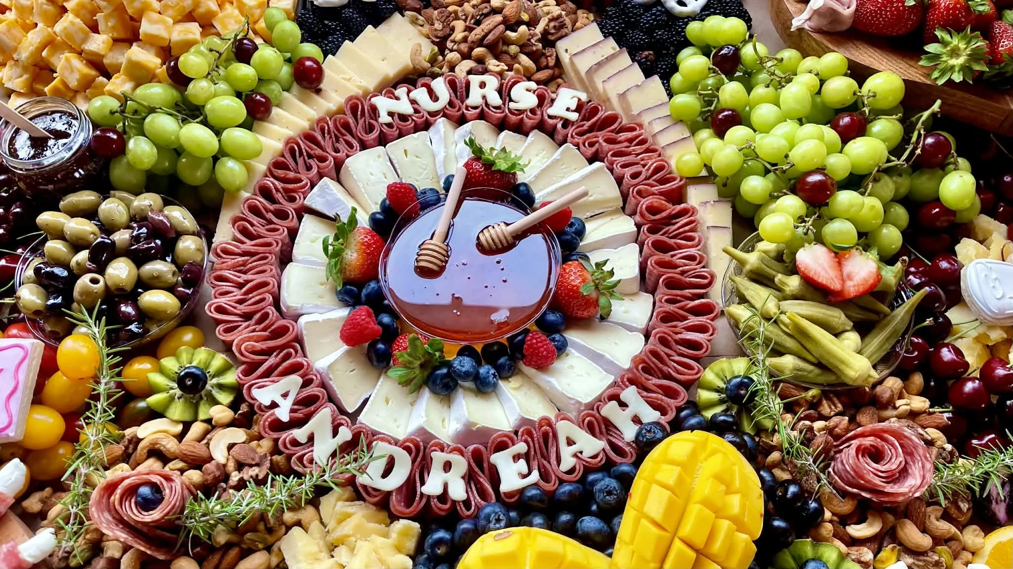 Charcuterie board set up with a varied selection of meats, cheeses, crackers and dips. Cheese letters cut out to spell Nurse Andreah goes around the center in a circle.