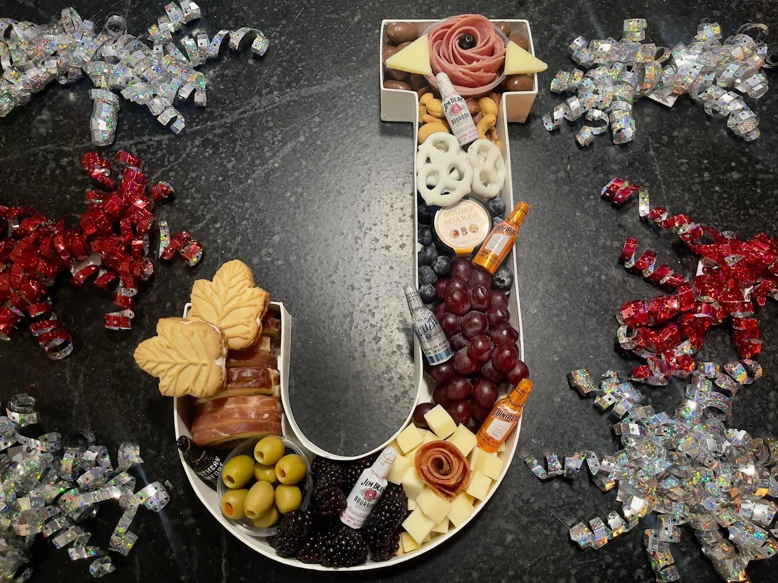 Overhead view of J shape charcuterie board featuring seasonal meats, cheeses and fruit.