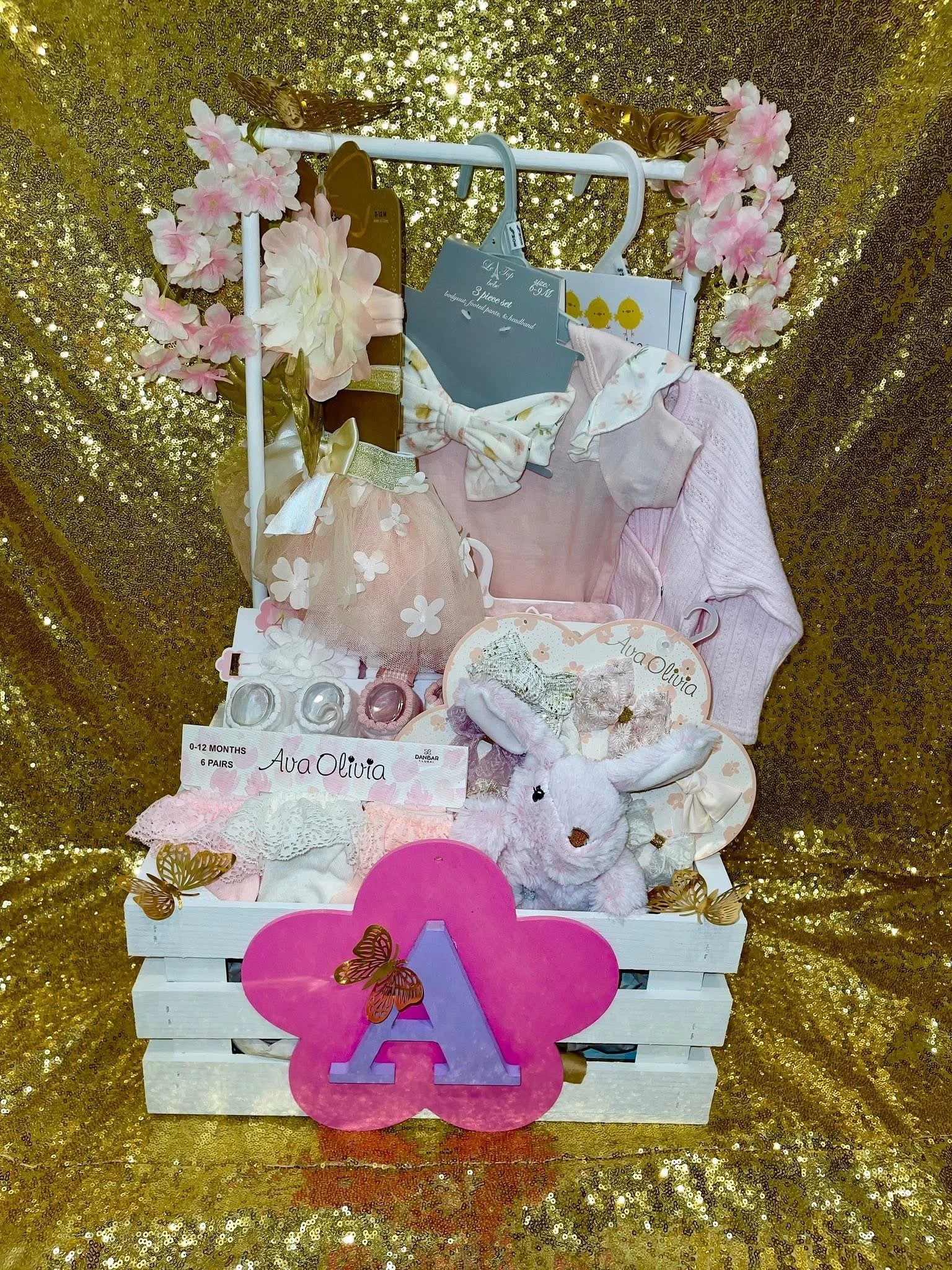 Front view of Littles Luxe Crate, featuring baby clothes, accessories and accents in pinks and white